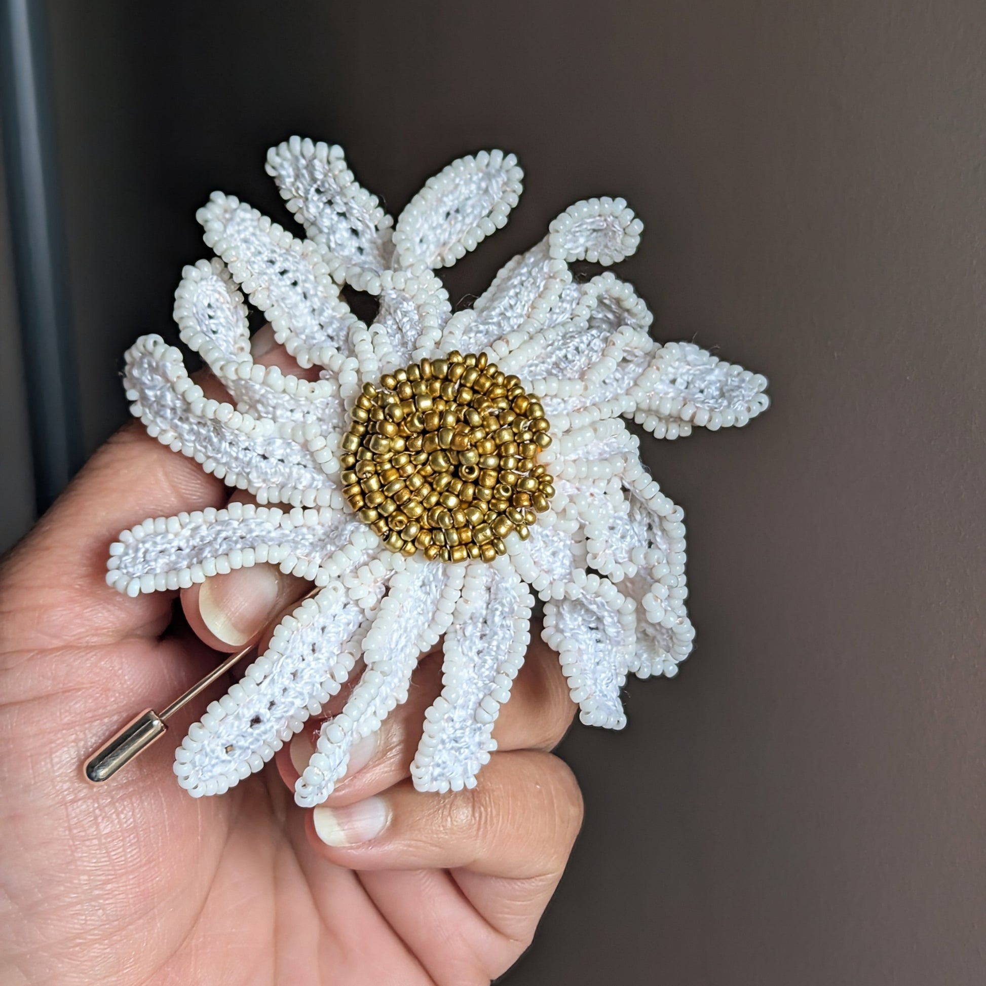 Daisy Garden of Becoming brooch held in palm featuring a handmade white crochet flower with duracoated gold bead centre by Mayaani Jewellery.