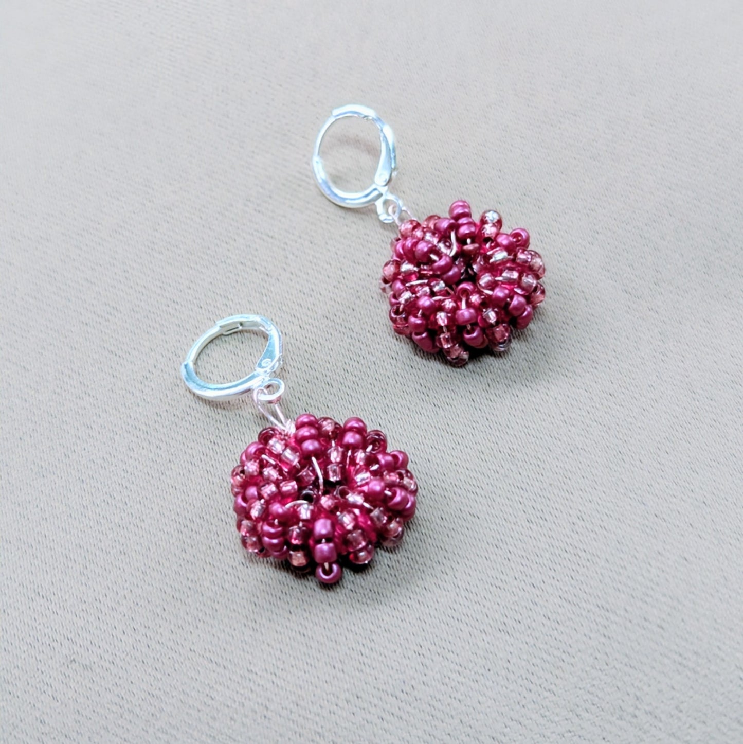Close-up of artisan-made pink seed bead earrings with sterling silver clasps and shimmering rose gold accents.