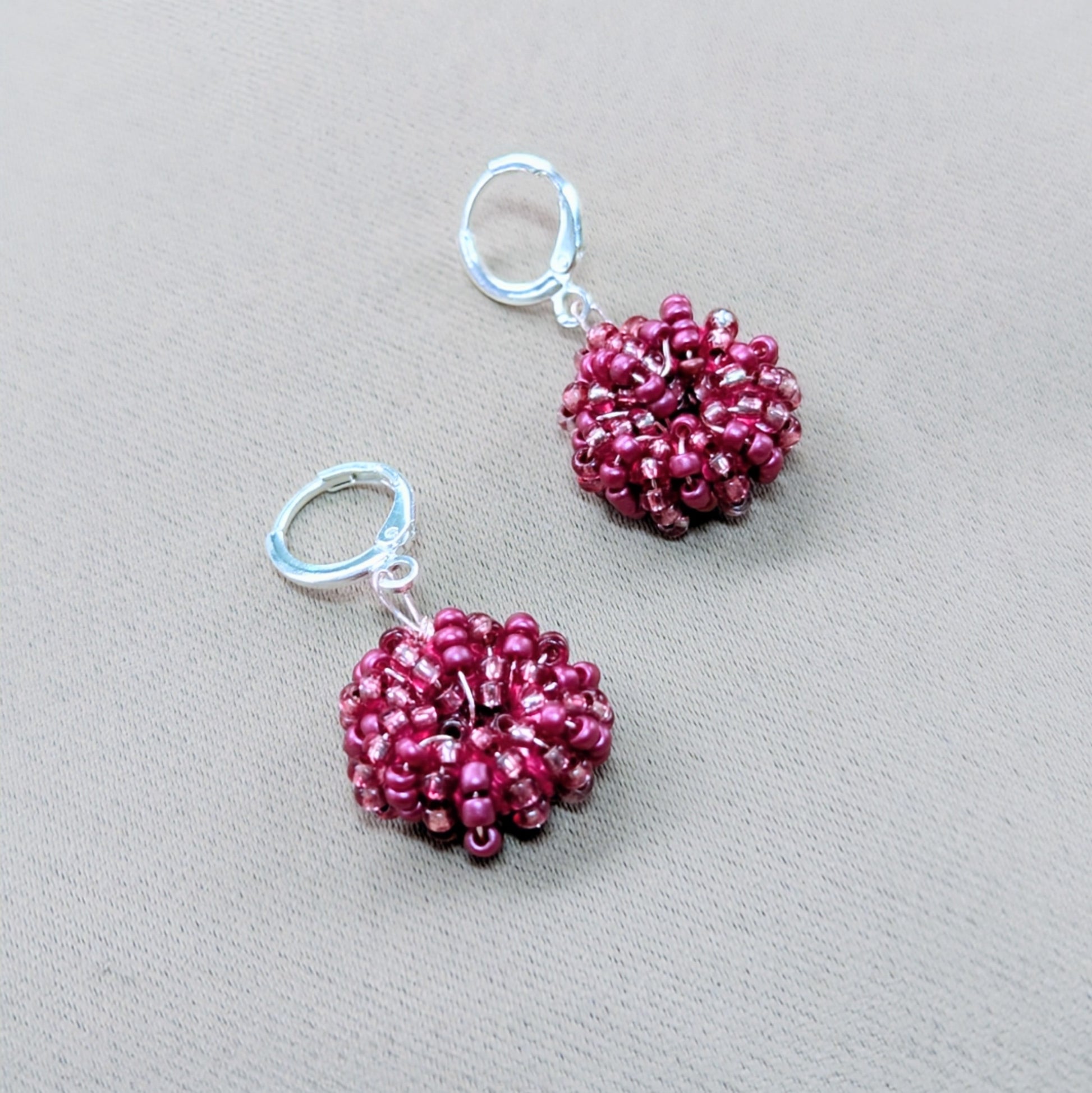 Close-up of artisan-made pink seed bead earrings with sterling silver clasps and shimmering rose gold accents.