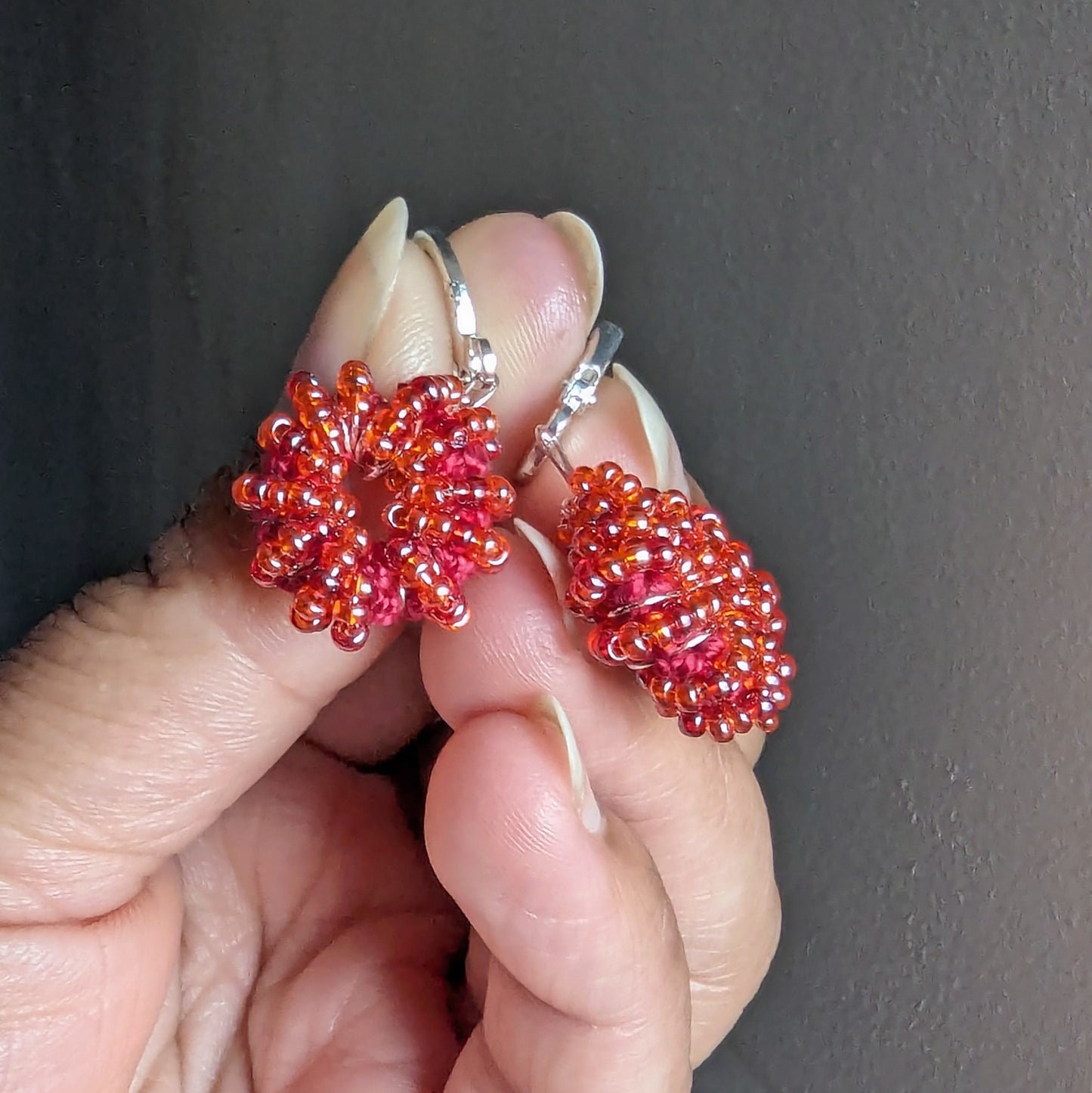 Hand holding orange-red handmade beaded earrings crafted by Mayaani Jewellery UK.