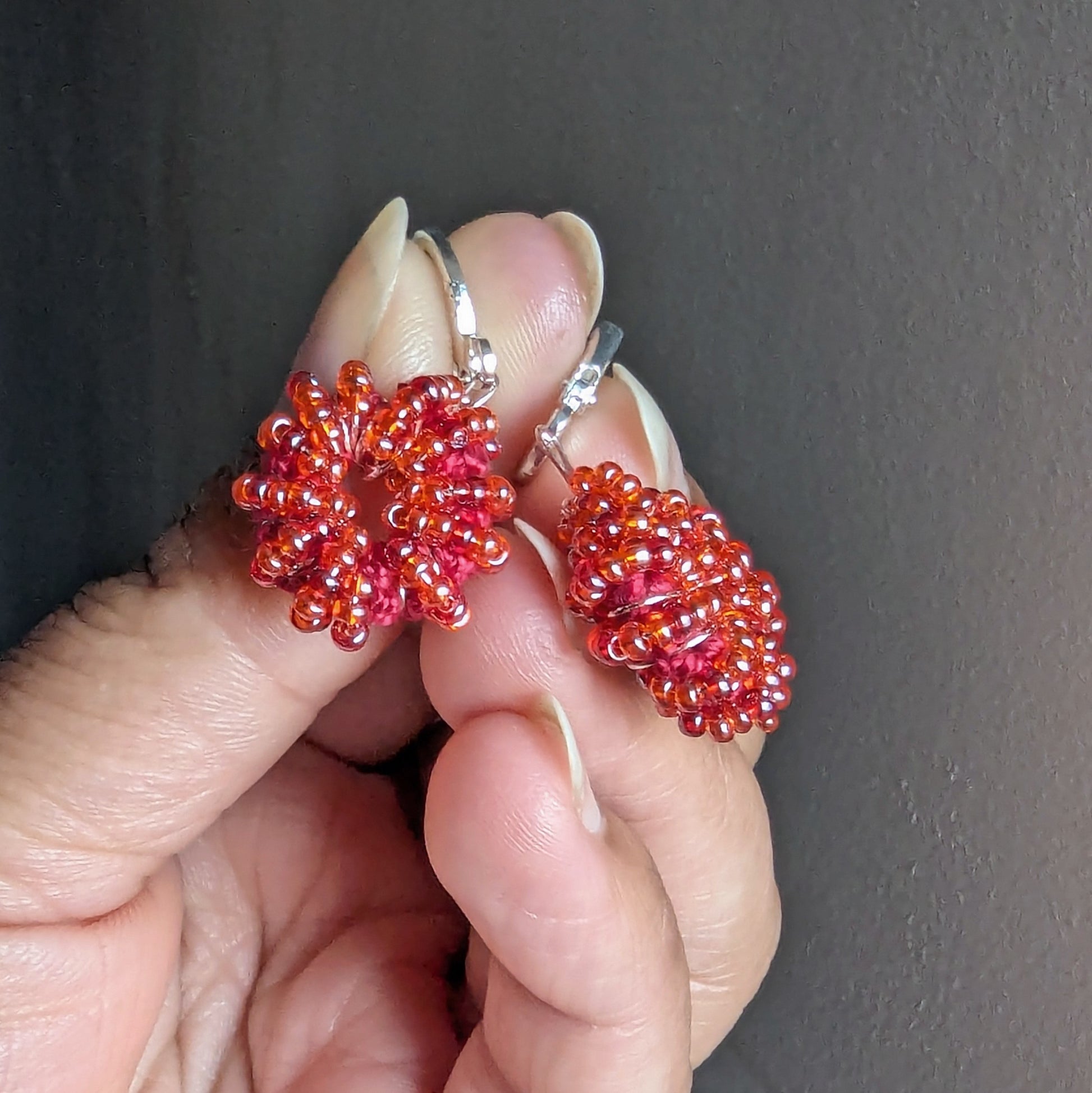 Hand holding orange-red handmade beaded earrings crafted by Mayaani Jewellery UK.