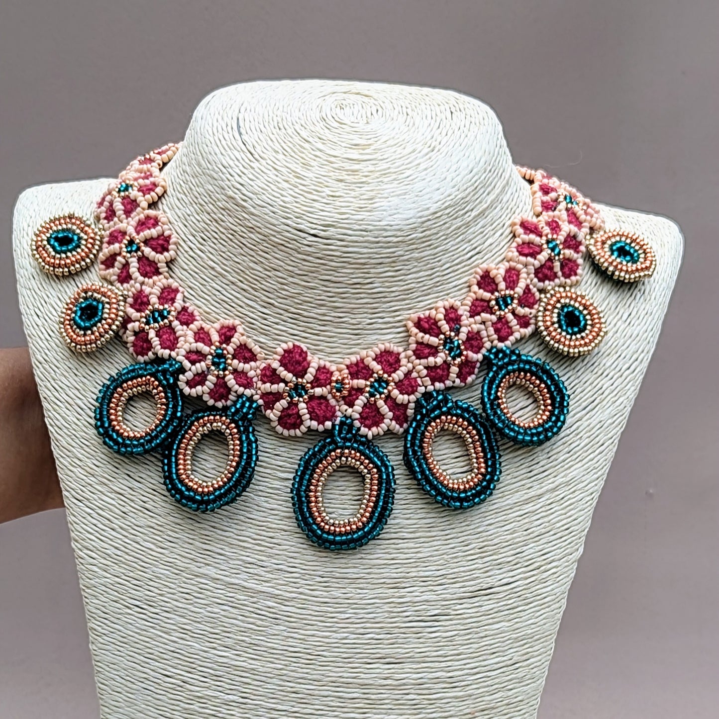 Displayed on a neck bust a statement Indian bridal necklace in red, peach and emerald green with gold accents artisan made in the UK for sustainable brand Mayaani Jewellery.