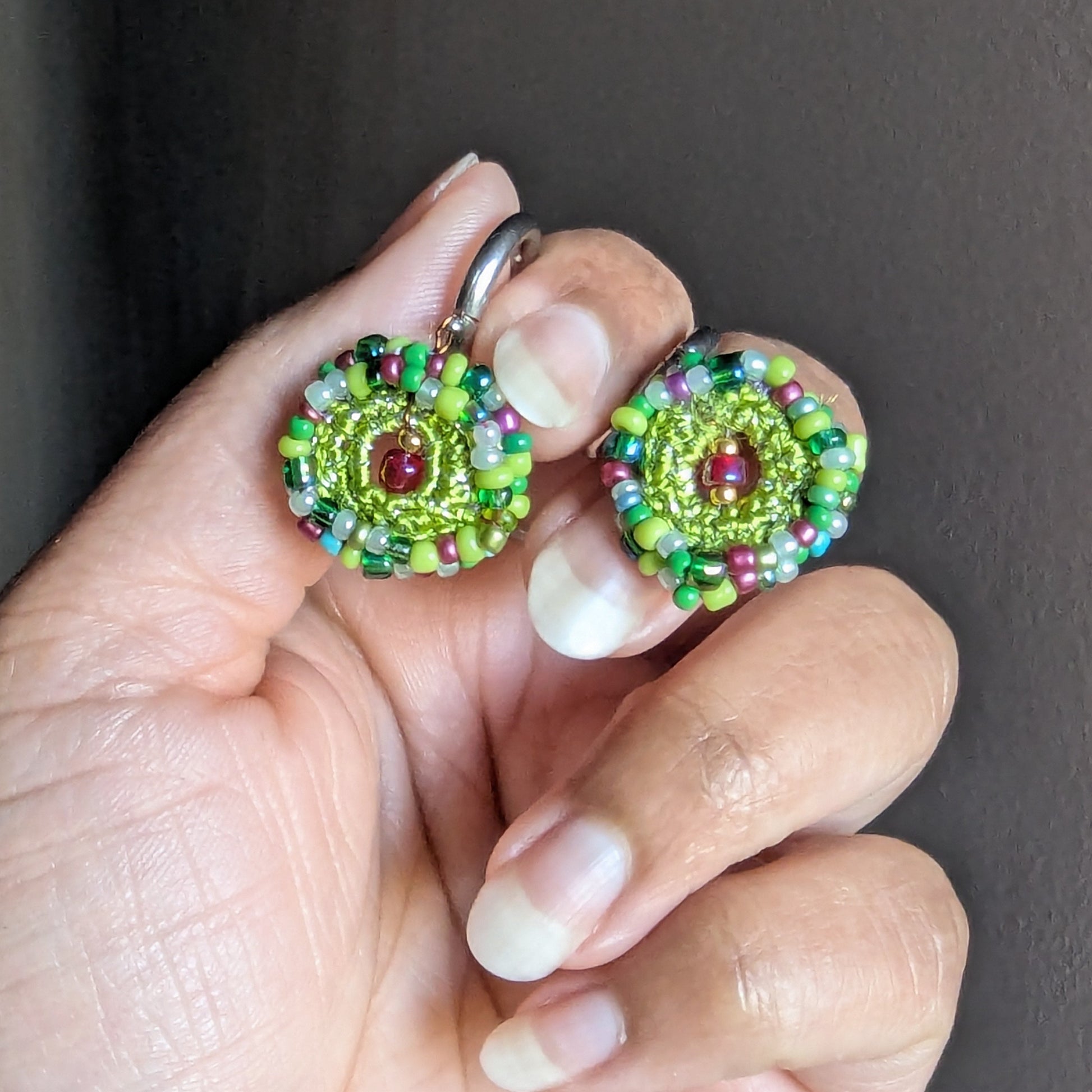 Close-up in hand view of Vana artisan earrings, showcasing fine bead crochet work, layered glass seed beads, and floral garden-like colour composition.