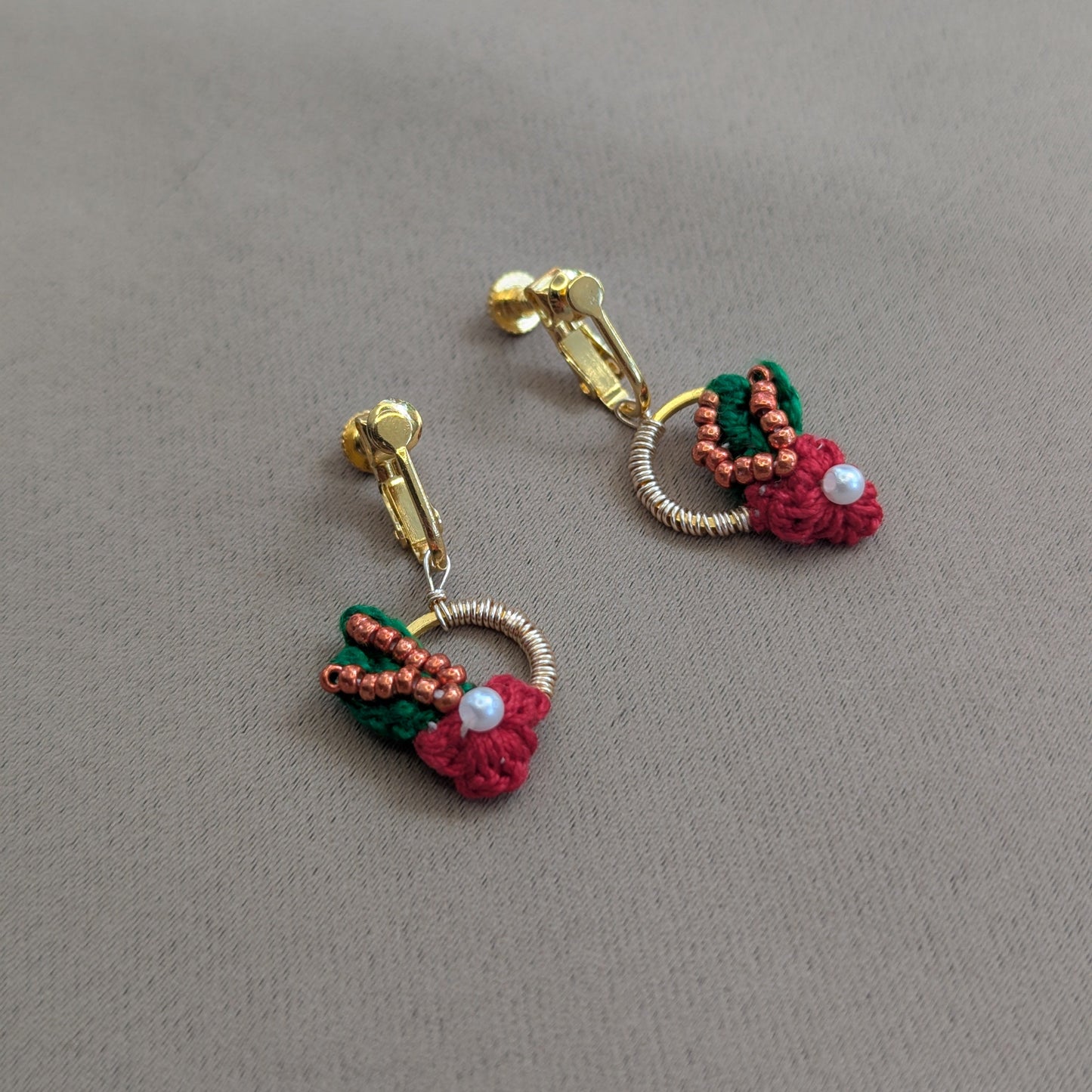 Flat lay view of a botanical inspired red, green, copper, pearl and gold clip-on pair of Kumkum designer handmade earrings exclusive to sustainable luxury brand Mayaani Jewellery UK.