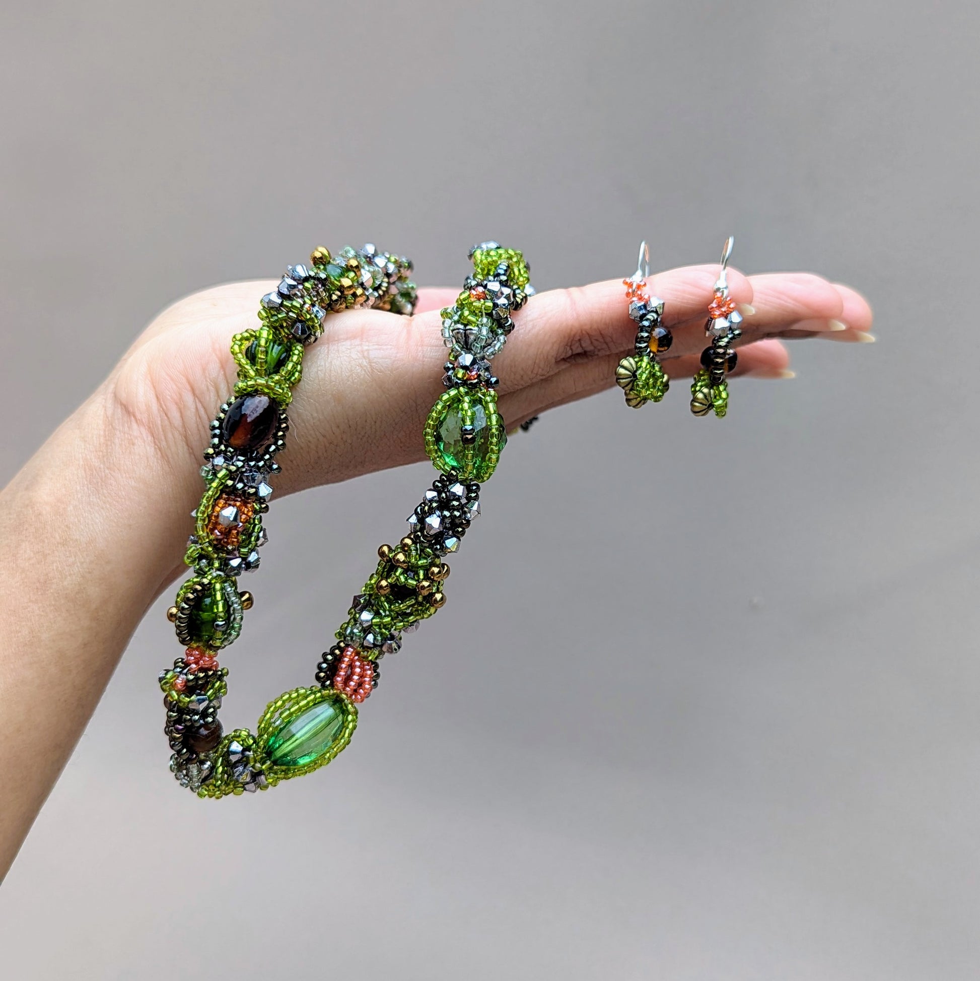 Hand holding a one-of-a-kind green beaded bracelet with matching earrings sustainably handcrafted for Mayaani Jewellery UK.