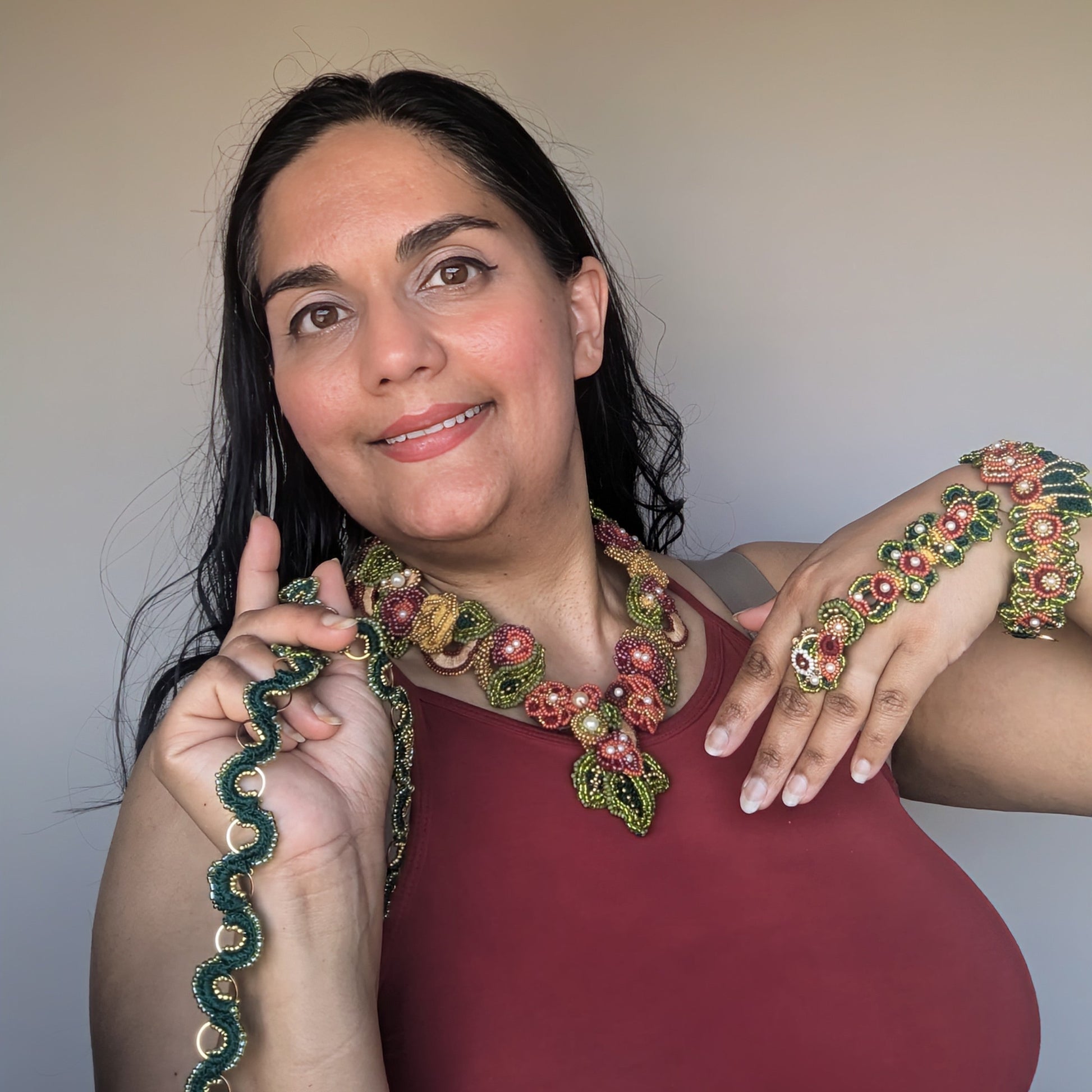 Megha of Mayaani Jewellery UK wearing the burgundy red, olive green and gold Rukmini necklace with 5-in-1 Indian hand bracelet whilst holding the custom chain in her hand.