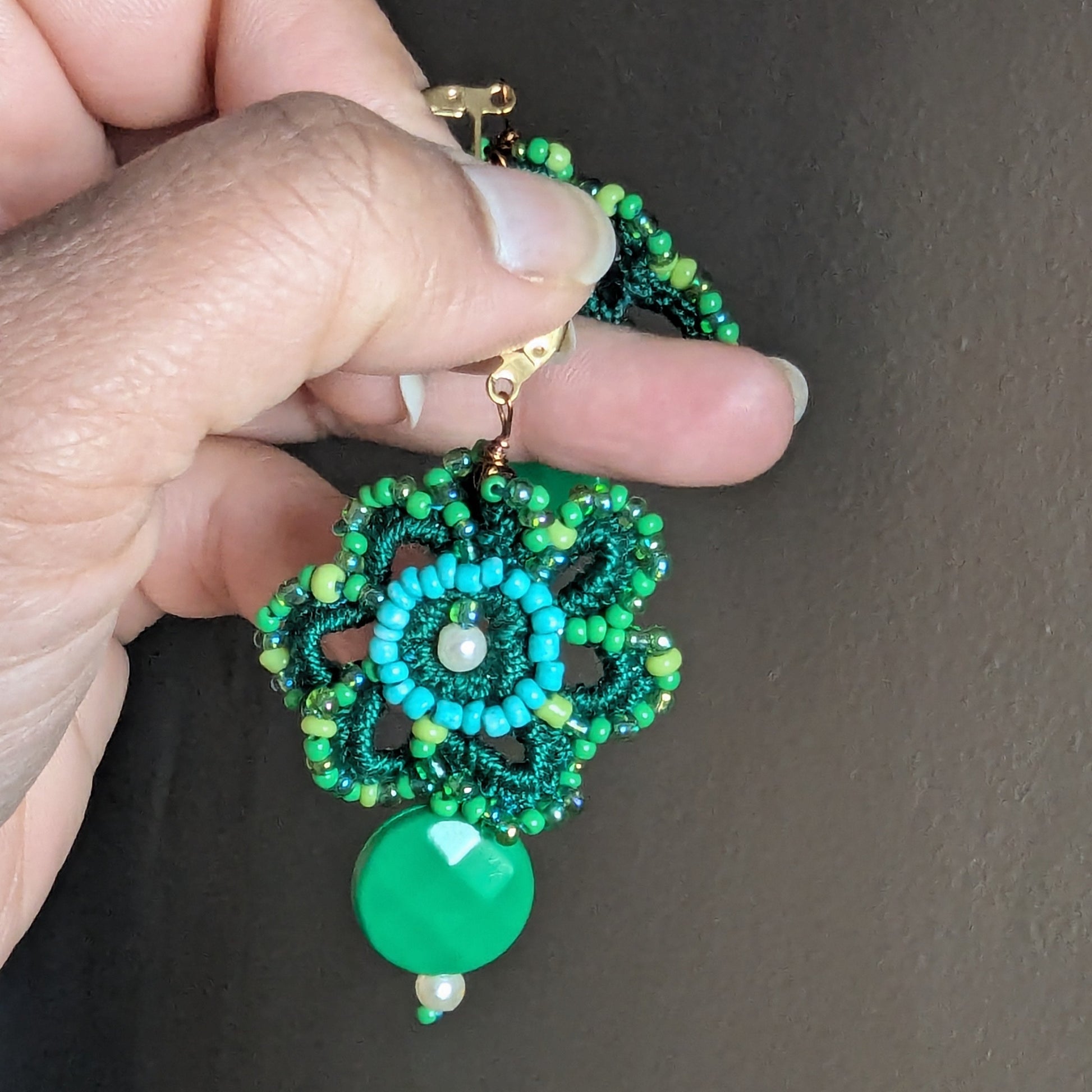 Green handcrafted floral earrings with vintage seed pearls and glass beads, shown held against a neutral background.