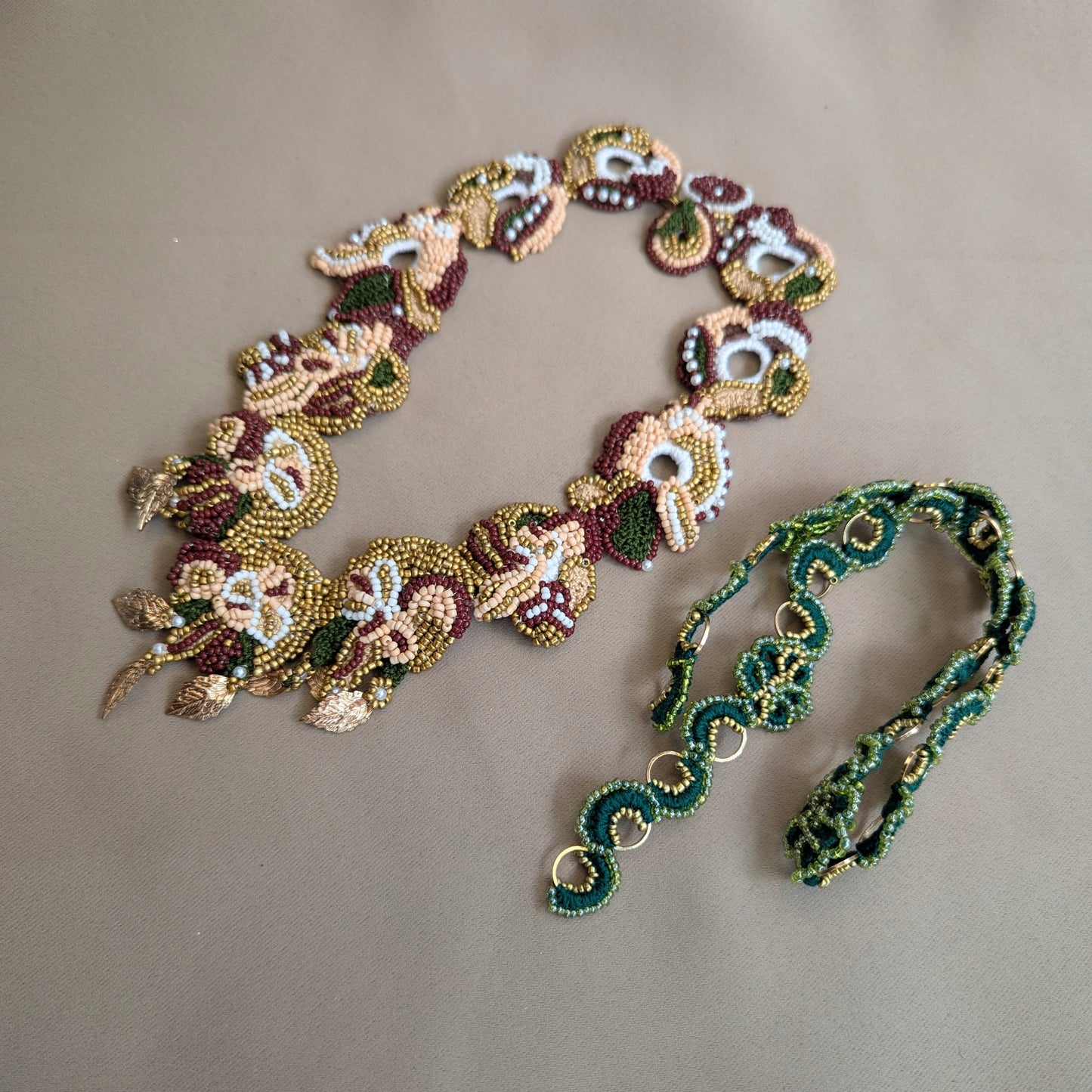 Flat lay view of the Aishwarya red, green, gold statement botanical necklace pictured alongside the Rukmini custom order emerald green and gold chain compatible with Aishwarya's detachable central pendant.