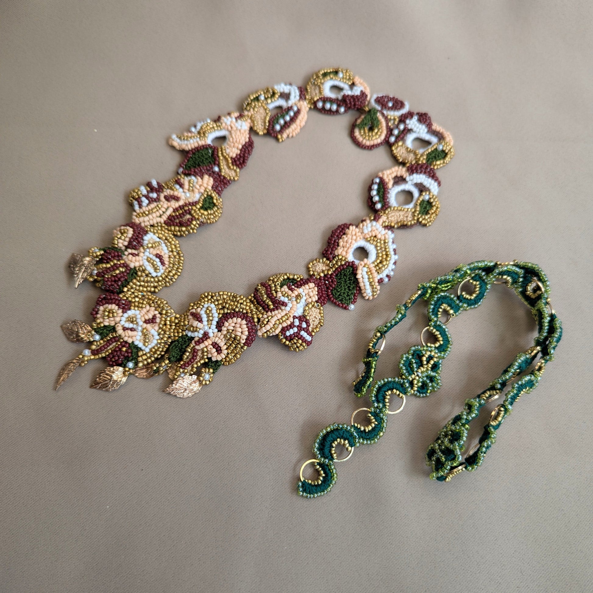 Flat lay view of the Aishwarya red, green, gold statement botanical necklace pictured alongside the Rukmini custom order emerald green and gold chain compatible with Aishwarya's detachable central pendant.