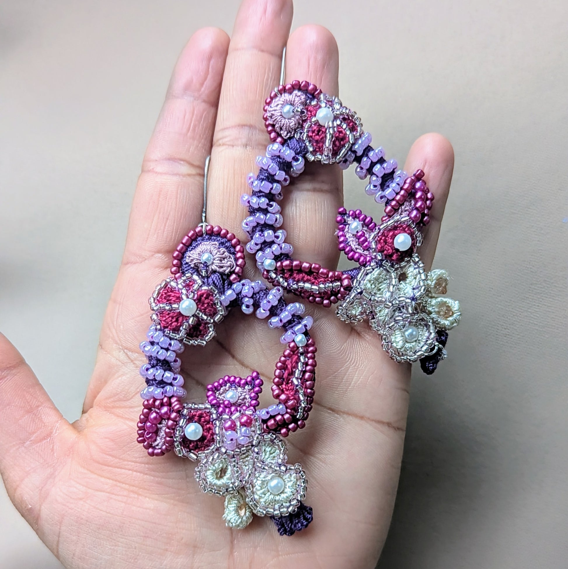 Close-up of Mayaani Jewellery's 'Gulab Rani' bridal earrings, handcrafted with glass seed beads in shades of red, purple, and ivory. The floral-inspired design features intricate bead embroidery and crochet, with layered textures and cascading beadwork for statement bridal look.