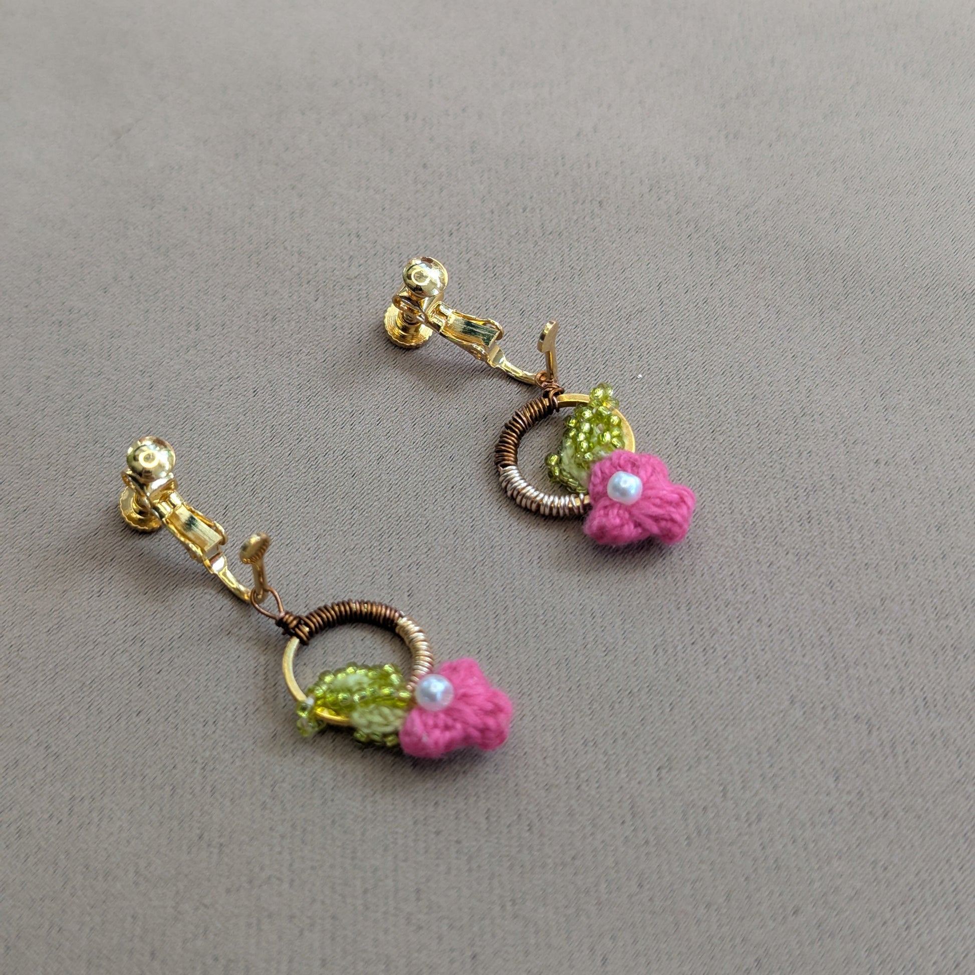 Flat lay view of an artisan handcrafted pair of Pallavi clip-on earrings exclusive to Mayaani Jewellery featuring pink and chartreuse green floral motifs with rose gold, bronze, pearl and gold stainless steel accents.