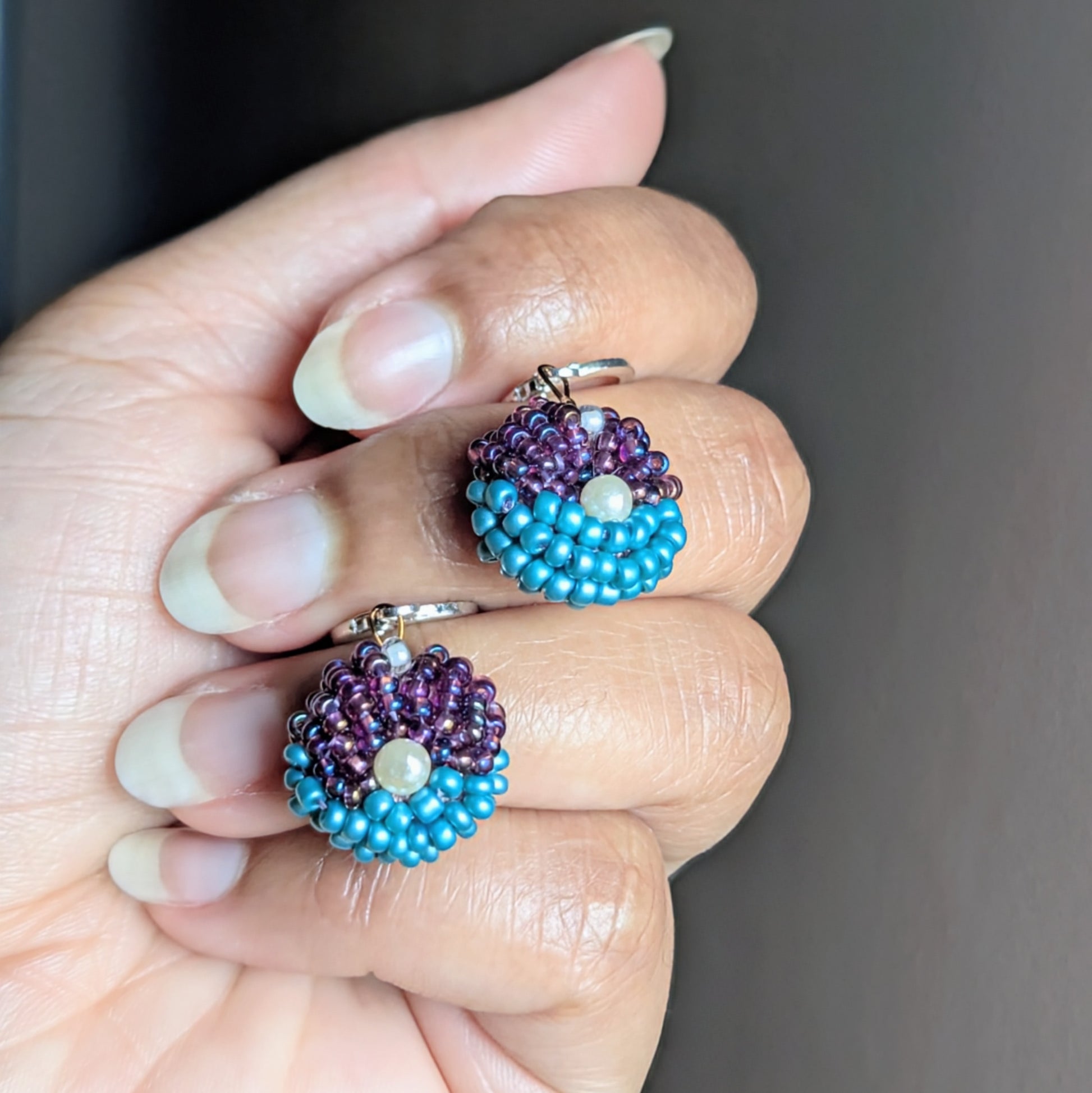 Hand holding Masi Lavanya earrings showing vibrant turquoise and amethyst beadwork with sterling silver clasps.
