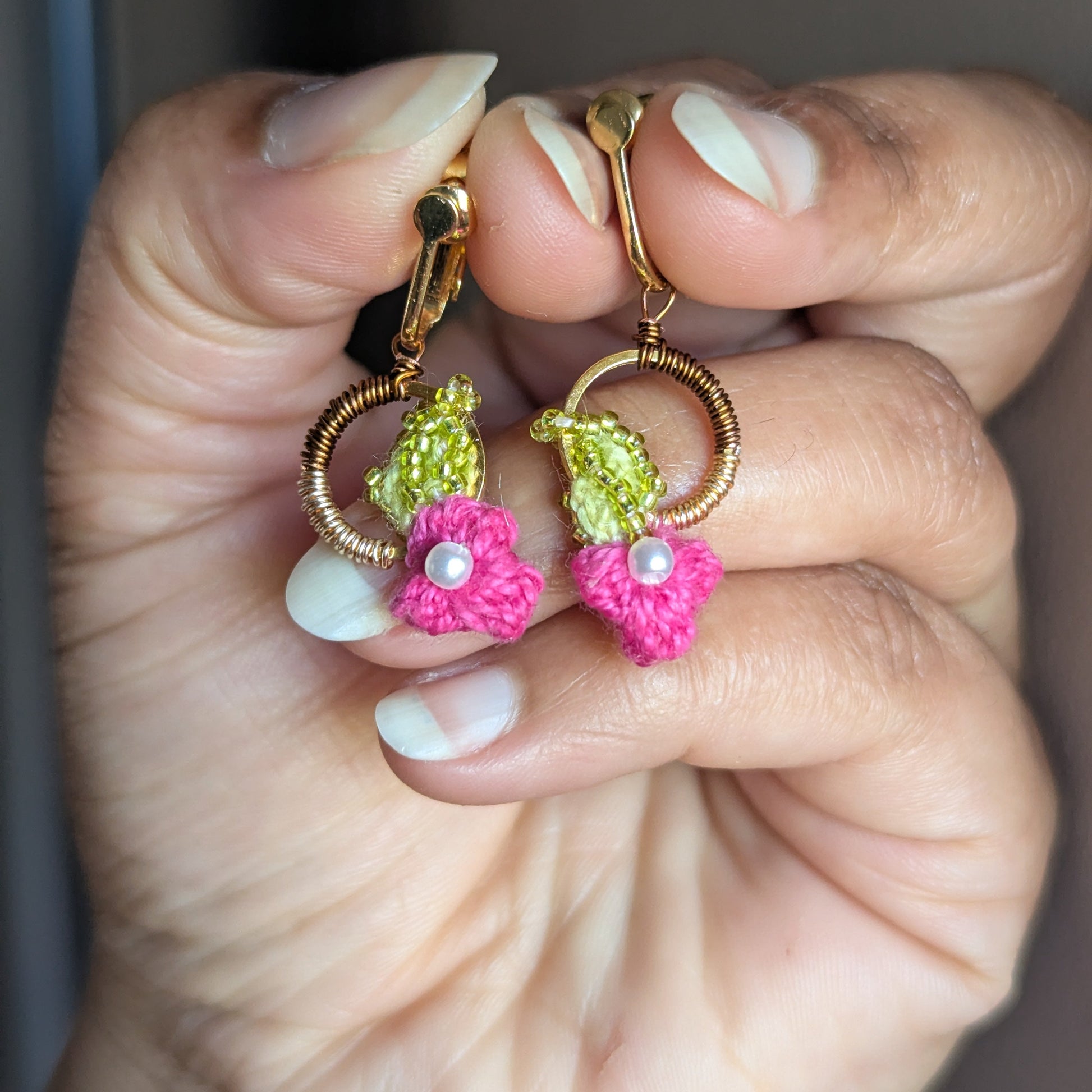 Hand holding a one of a kind pair of Pallavi lightweight comfortable clip on earrings by sustainable luxury brand Mayaani Jewellery UK featuring floral motifs and accents in pink, chartreuse green, pearl and gold.