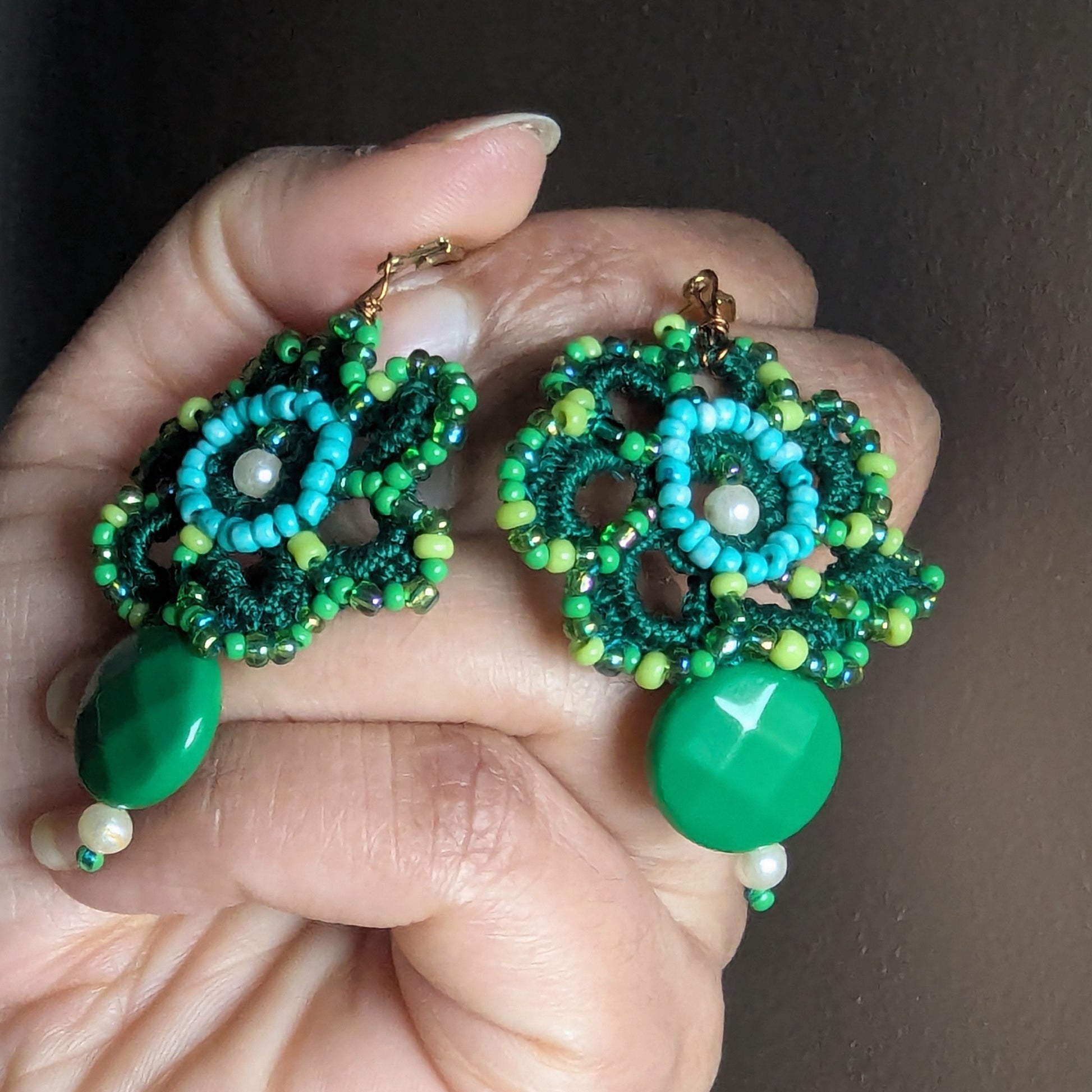 Handmade green floral crochet earrings held in hand featuring vintage seed beads, Czech glass beads and gold stainless steel clasps.