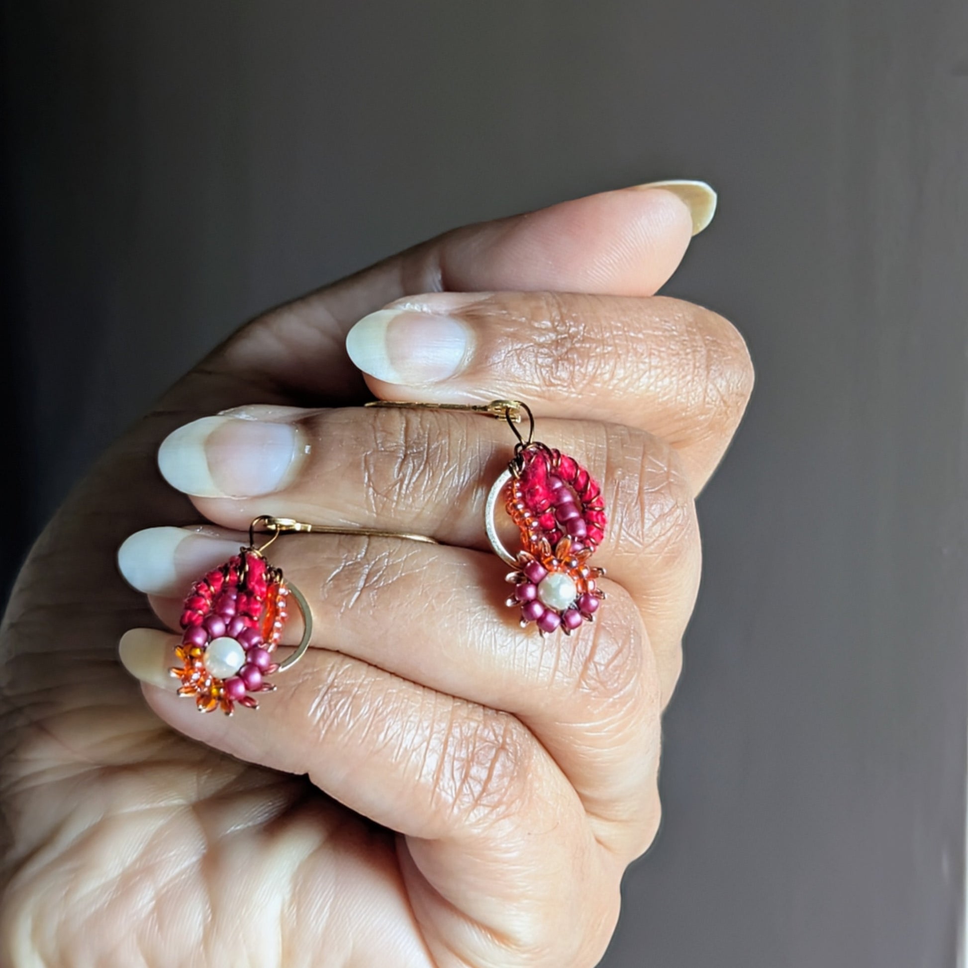 Hand holding Lalima red and gold handmade Indian earrings with crochet and beadwork.