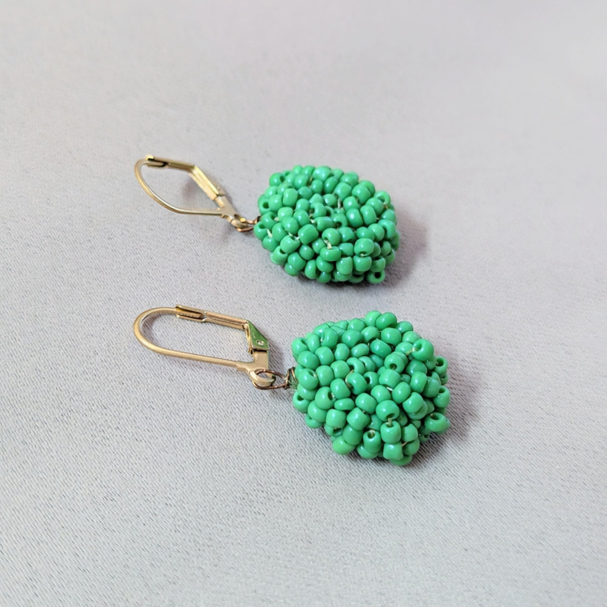Pair of Masi Harita green earrings displayed on neutral background highlighting their vibrant handmade texture.