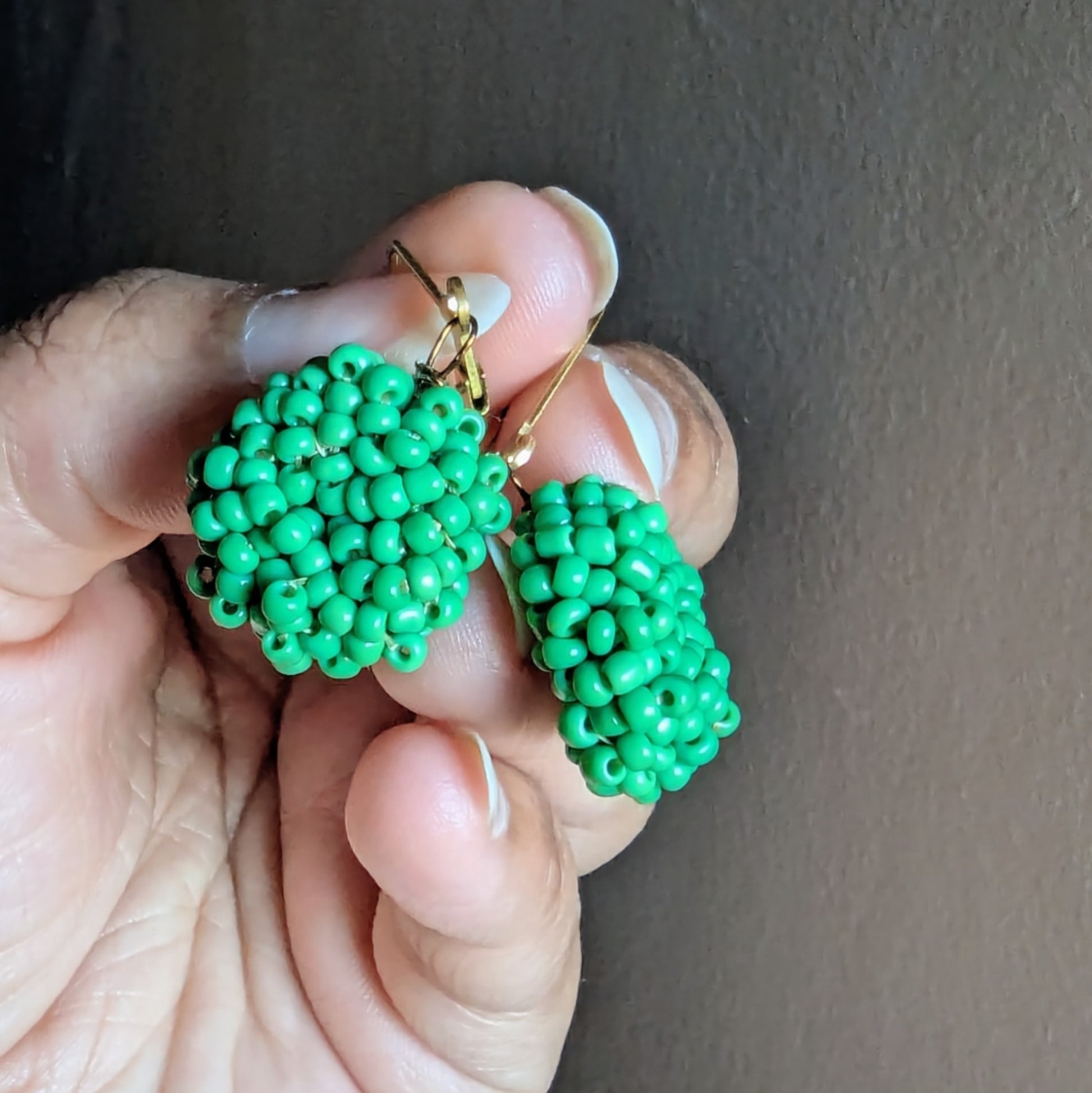 Close-up of green beaded earrings showing gold stainless-steel clasps and meticulous wire craftsmanship.
