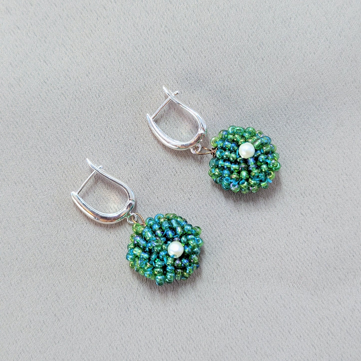Pair of green beaded earrings displayed on neutral background, symbolising renewal and slow craftsmanship.