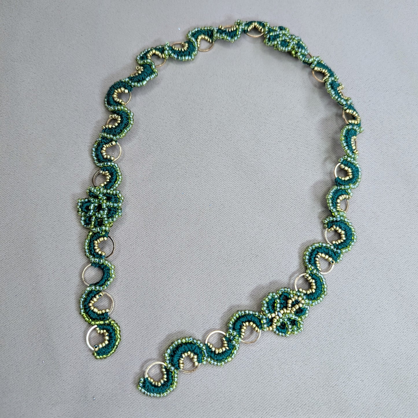 Handmade Rukmini beaded chain in emerald green, pearl cotton and gold stainless steel hoops lying flat on a neutral fabric backdrop. Made to order by Mayaani Jewellery UK.