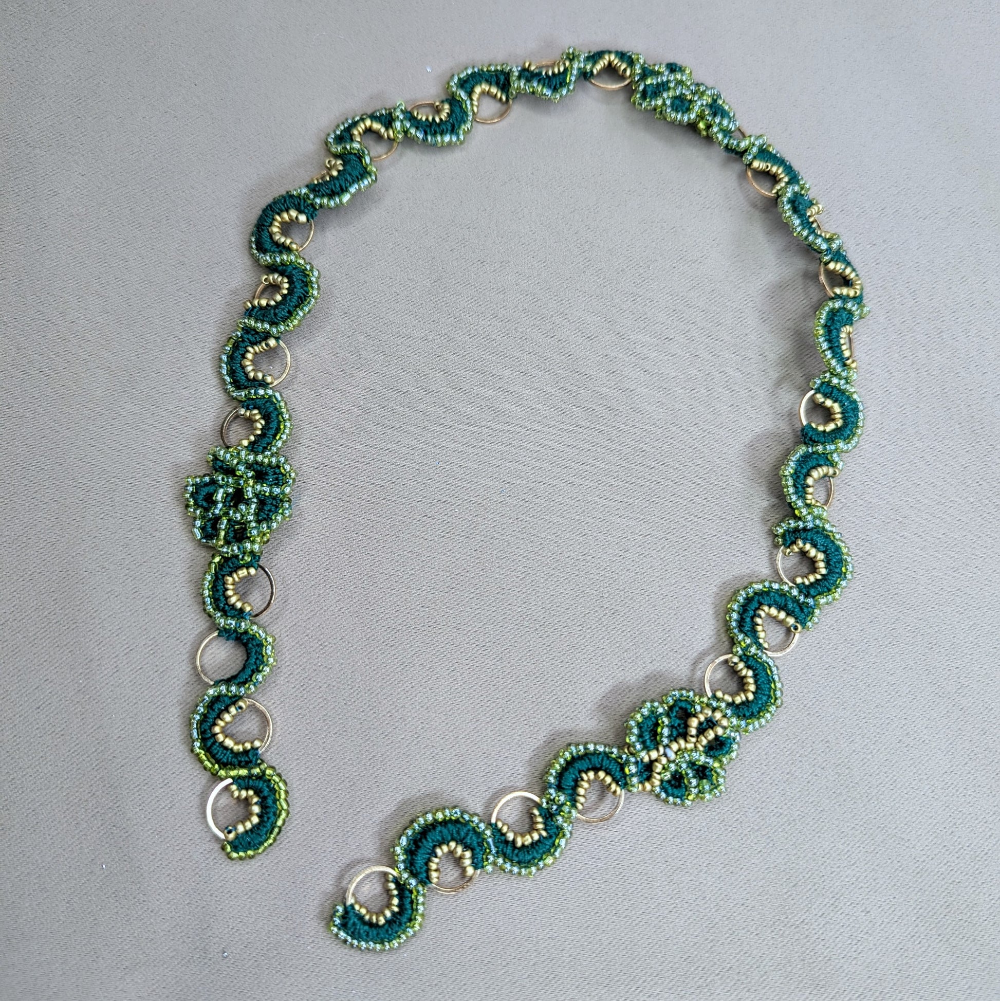 Handmade Rukmini beaded chain in emerald green, pearl cotton and gold stainless steel hoops lying flat on a neutral fabric backdrop. Made to order by Mayaani Jewellery UK.