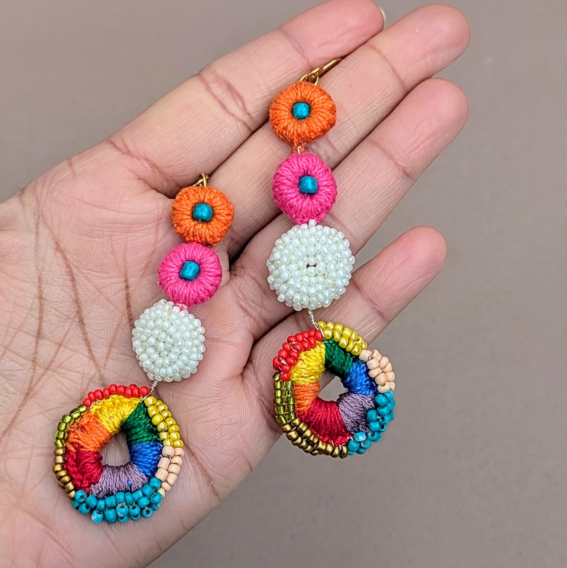 Vibrant multicolour crochet bridal earrings handmade by Mayaani Jewellery, featuring circular drop design with pink, orange, white, and rainbow beadwork on a grey background.