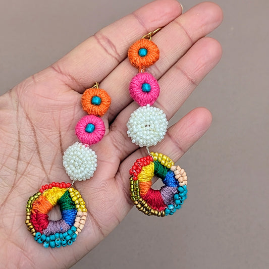 Vibrant multicolour crochet bridal earrings handmade by Mayaani Jewellery, featuring circular drop design with pink, orange, white, and rainbow beadwork on a grey background.