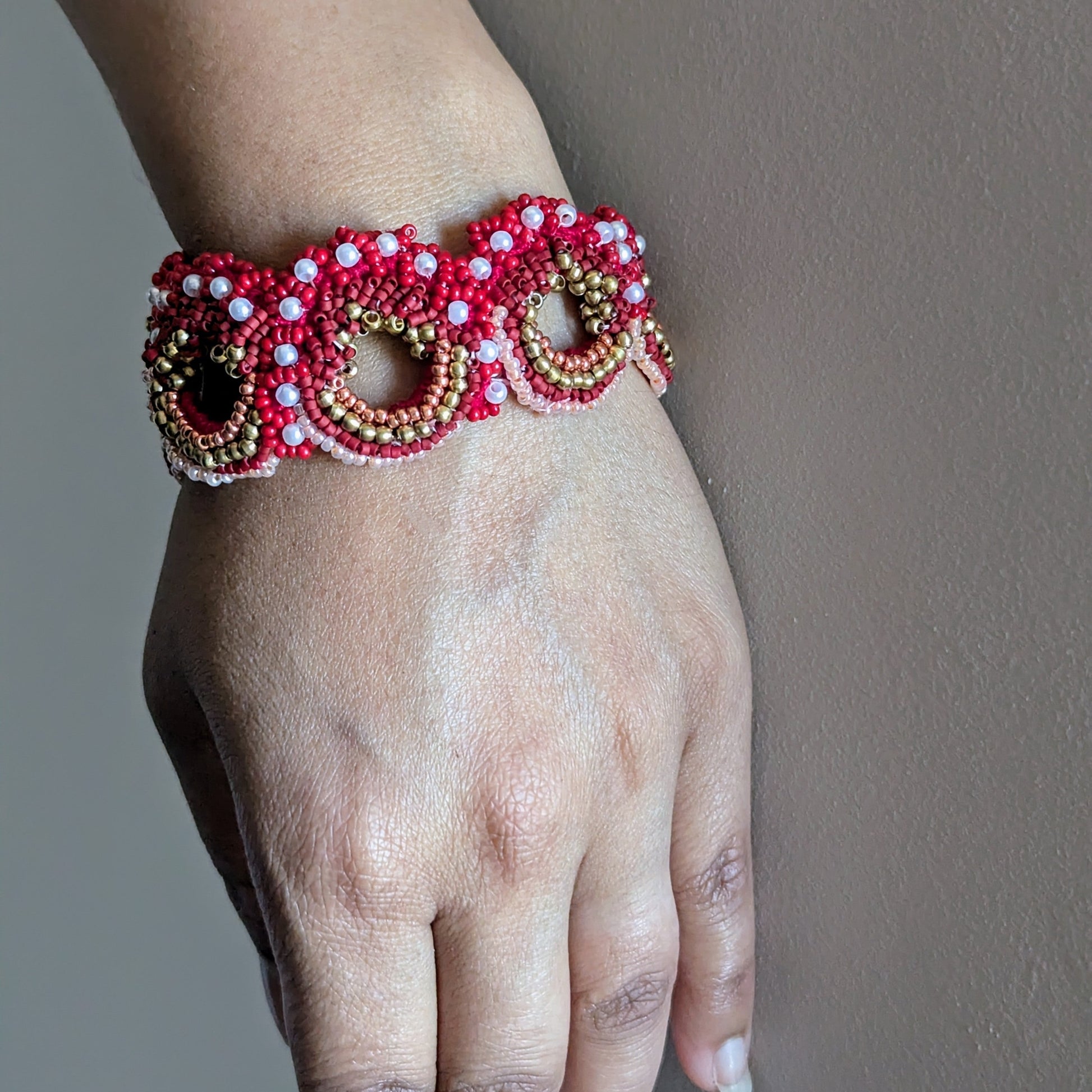 Close up view of a hand wearing the red gold and pearl designer Shreya bracelet element against a neutral grey backdrop.