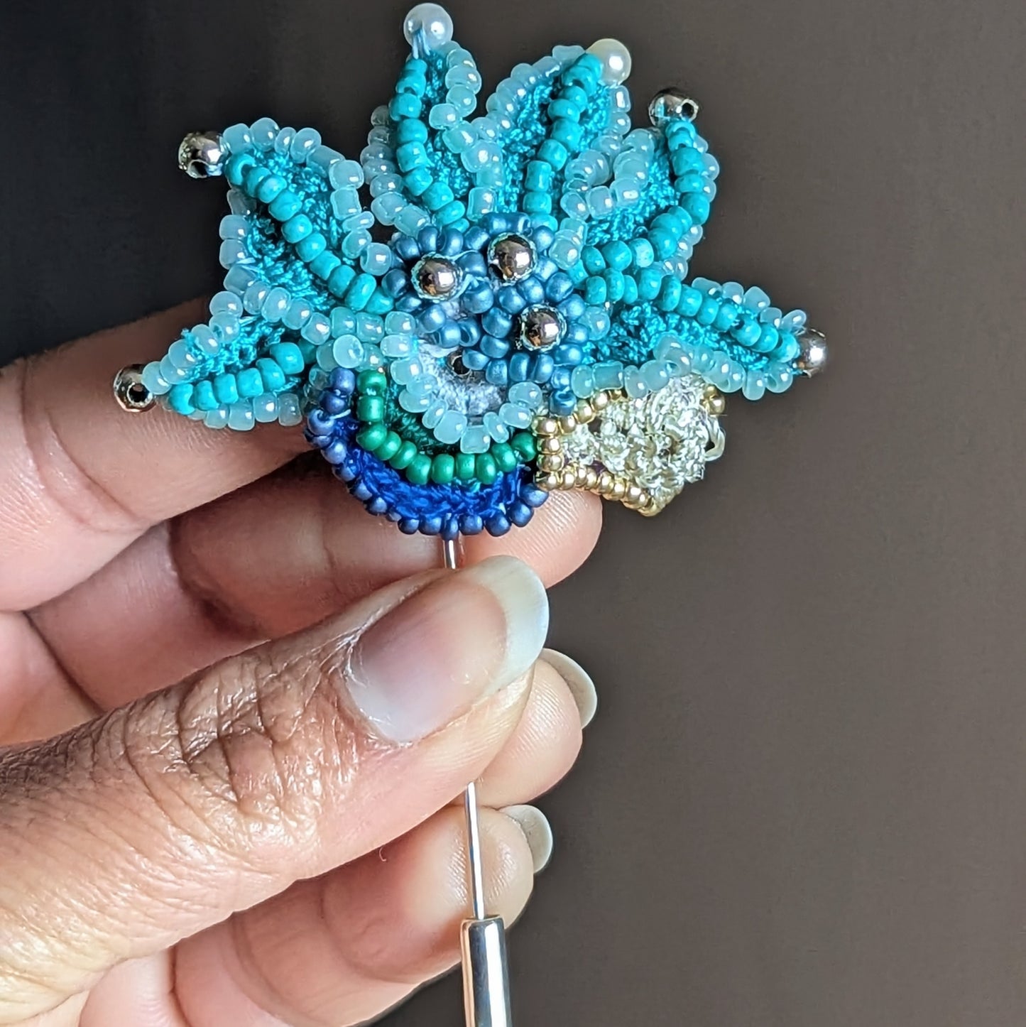 Close up view of Jalika handmade textile brooch in hand highlighting intricate turquoise beadwork, sculptural embroidery and sustainable craftsmanship.