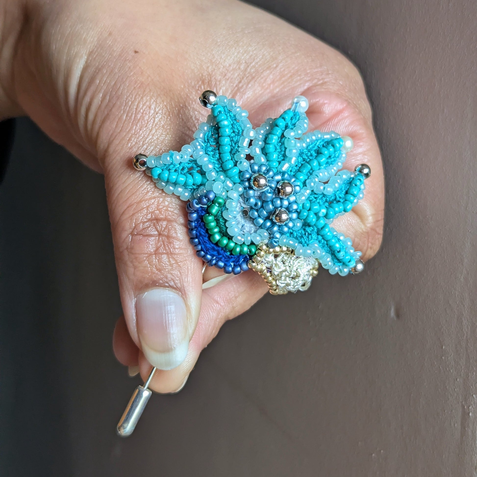 Handcrafted turquoise beaded brooch Jalika displayed in hand showcasing vintage glass seed bead and silver accent bead embroidery coupled with delicate hand crochet finished with a stainless steel brooch pin.