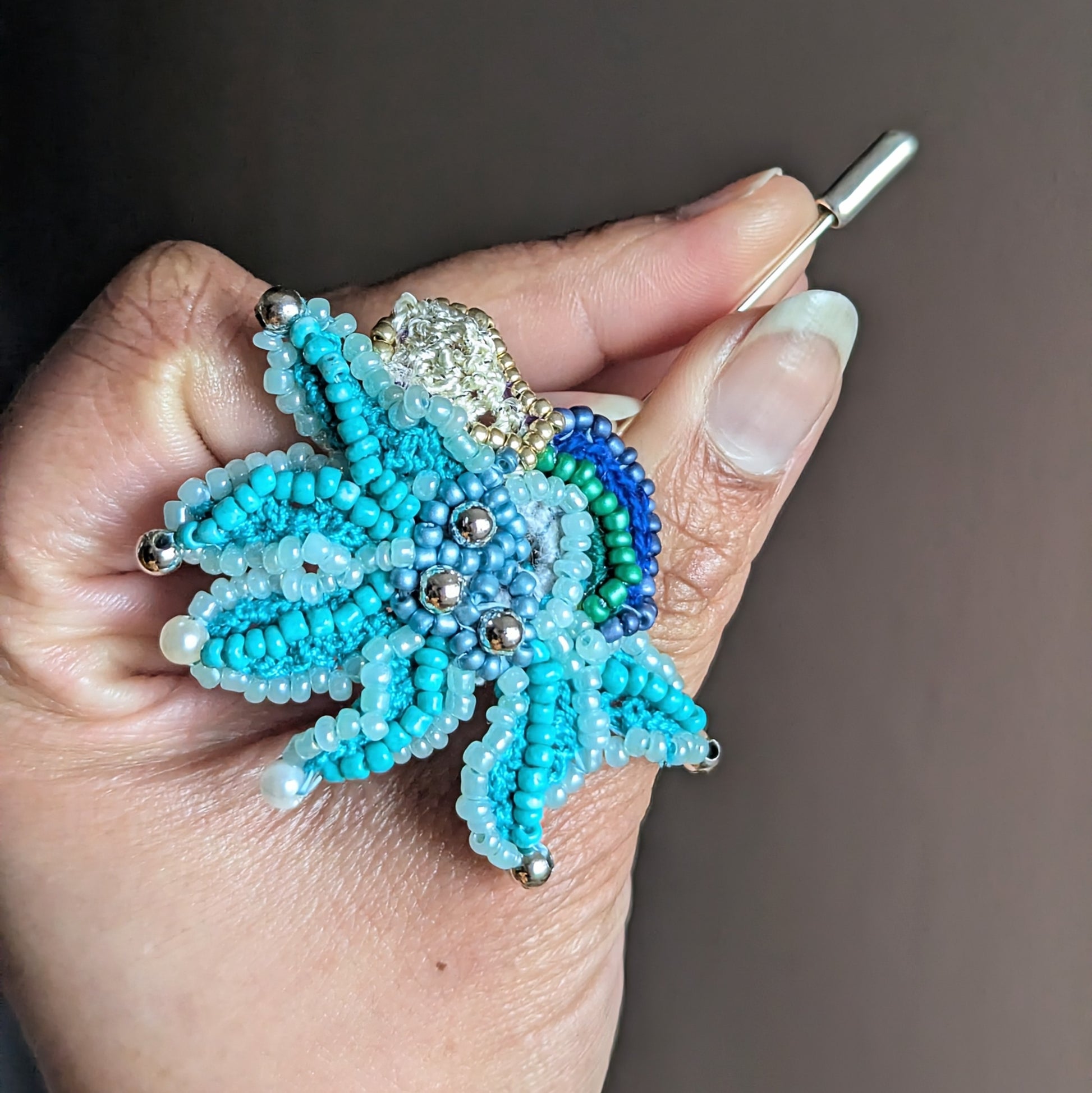 Angled view of a hand holding the handcrafted artisanal Jalika brooch, one of a kind showcasing intricate workmanship and expert attention to design composition and detail. Sustainably slow handmade in the UK.