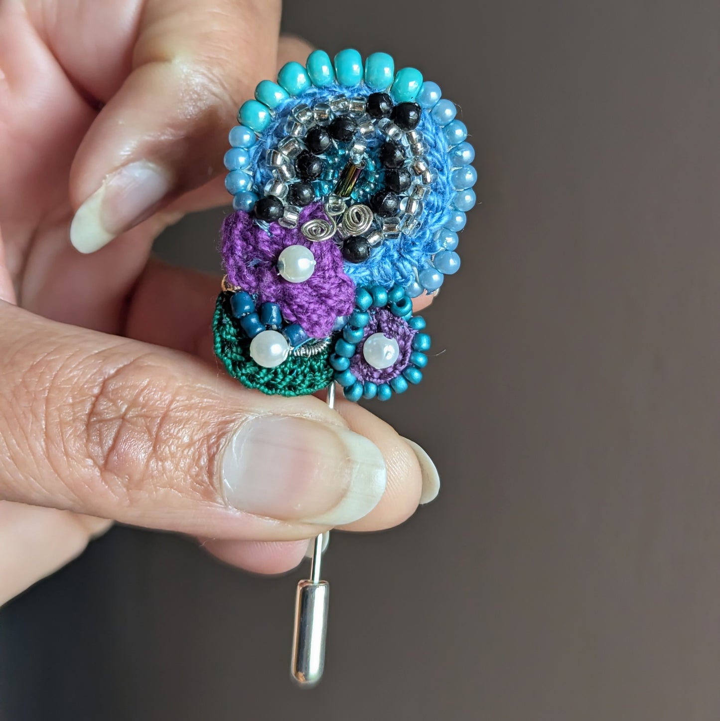 Kairavi handmade butterfly brooch with turquoise beadwork, purple crochet detail and reclaimed vintage beads held in hand.