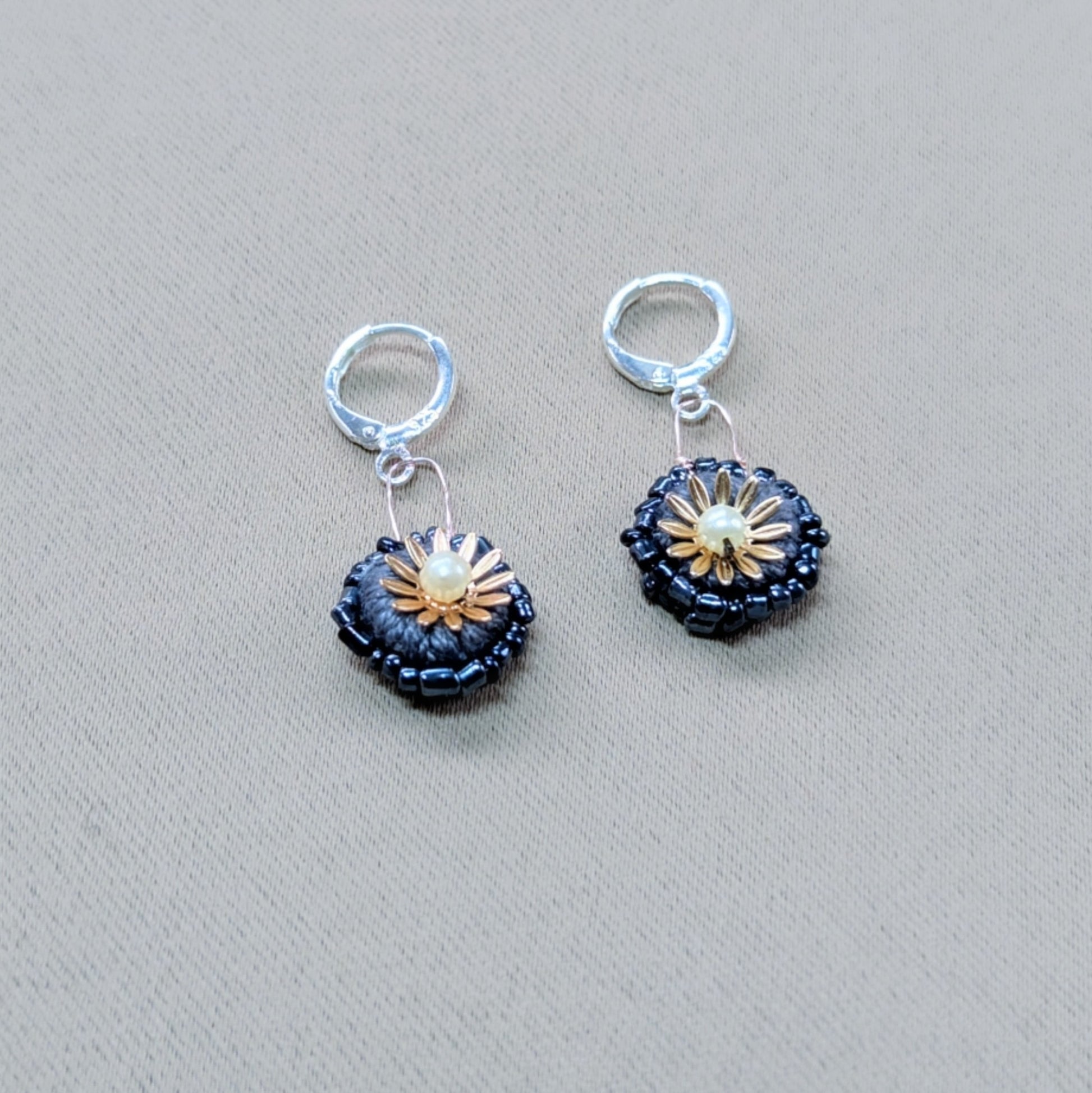 Close-up of a small pair of earrings - featuring hand crochet, bead and wire artistry on a soft grey fabric backdrop.