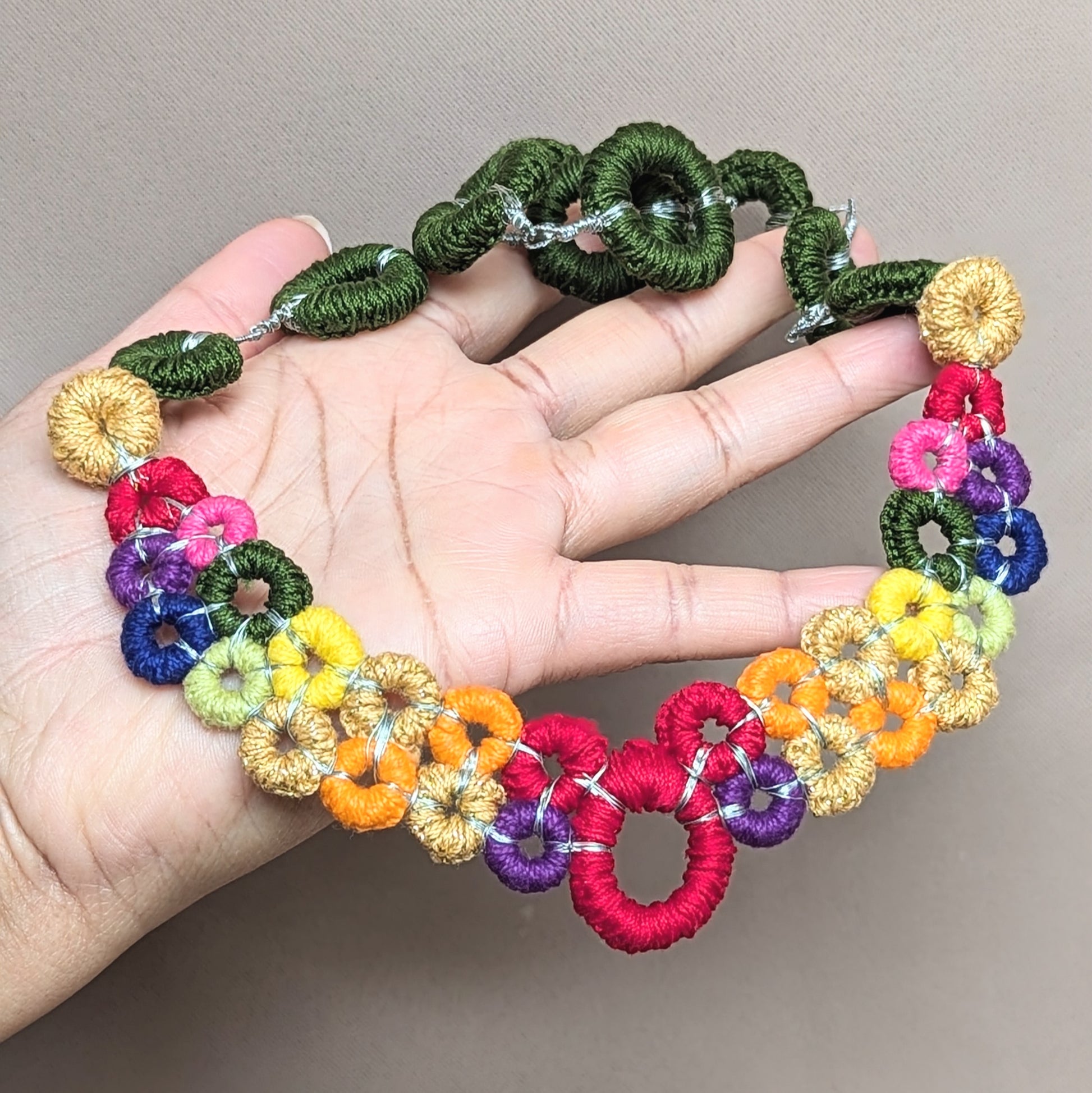 Handmade detachable rainbow necklace featuring crochet centrepiece, shown held in hand, one-of-a-kind modular jewellery handcrafted in the UK by Mayaani Jewellery.