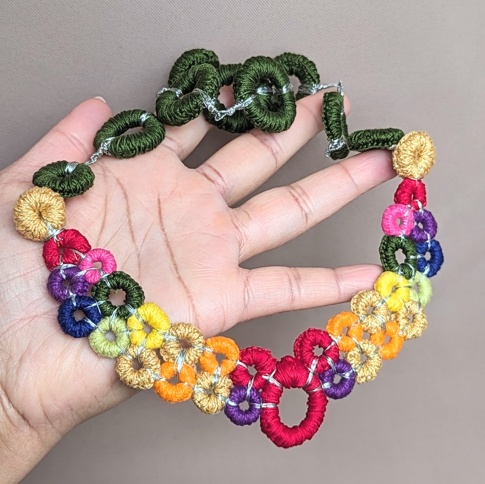 Rainbow centrepiece necklace resting in hand, featuring hand-crocheted circles and interchangeable chain design.