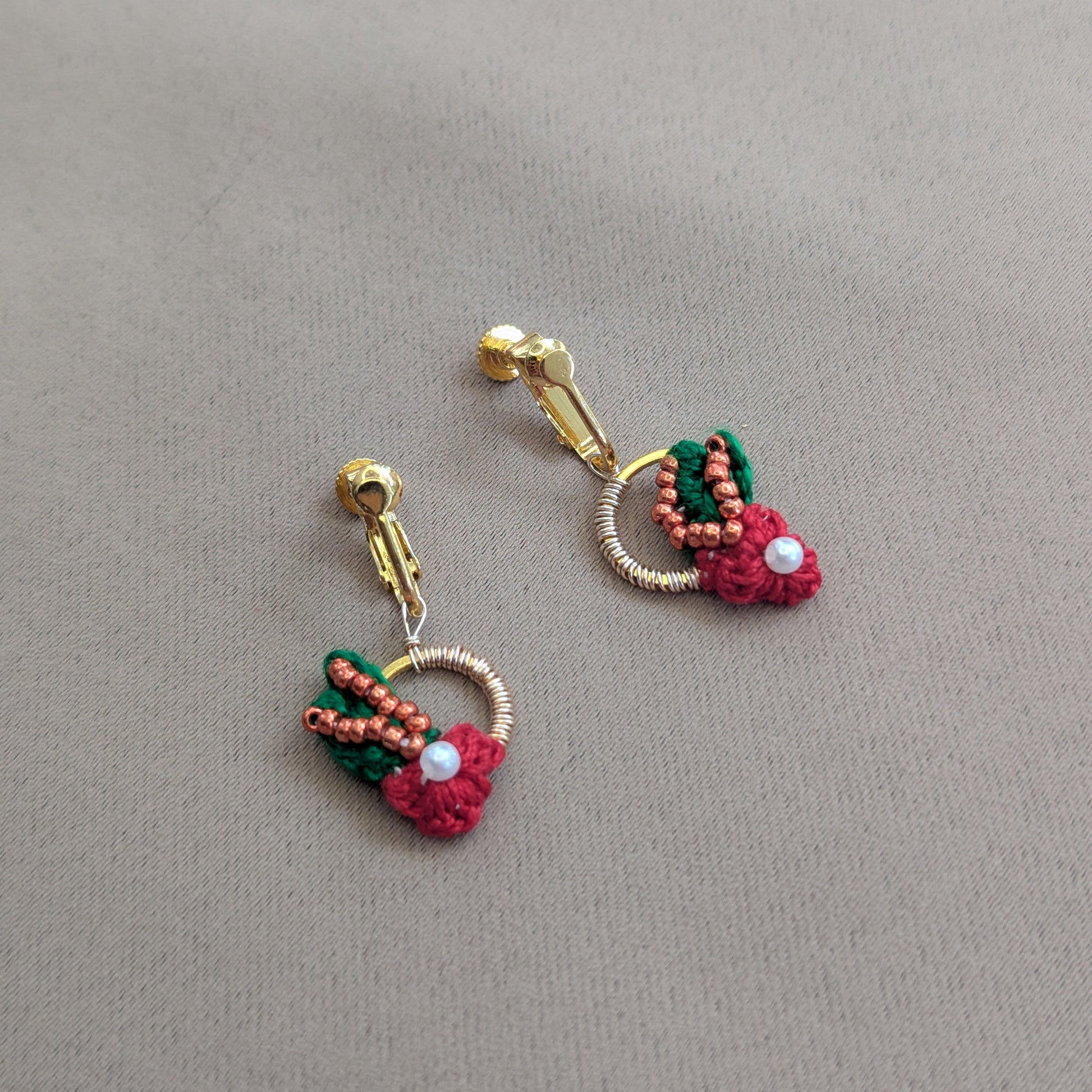 A one off pair of luxurious gold stainless steel hoop clip-on earrings in red, green, copper and gold tones with pearl accents handcrafted using a combination of hand crochet, hand wire artistry and hand bead embroidery unique to UK designer brand Mayaani Jewellery.