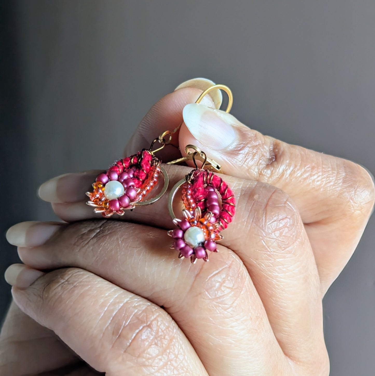 Close-up of red crochet hoop earrings with vintage seed pearls and gold floral accents.