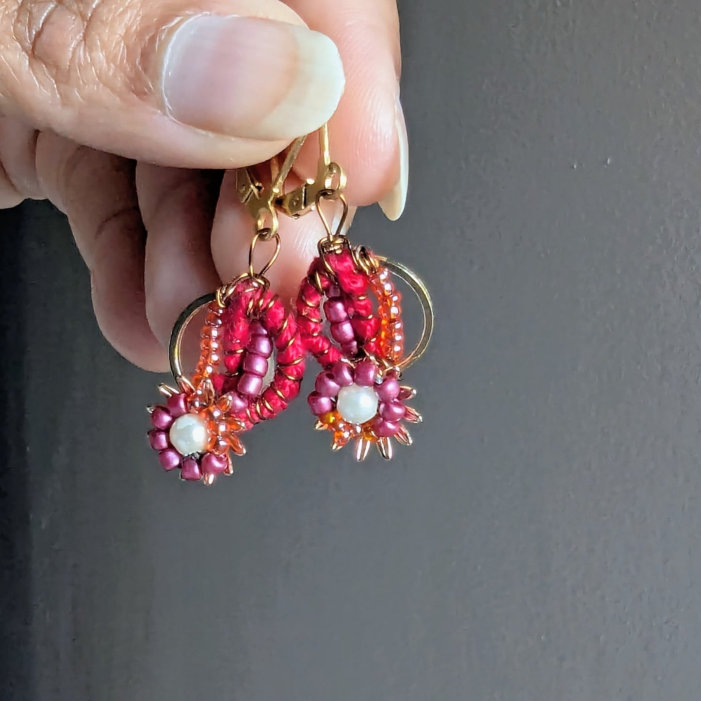 Artisan-made red and gold Indian earrings displayed in hand with intricate bead embroidery.