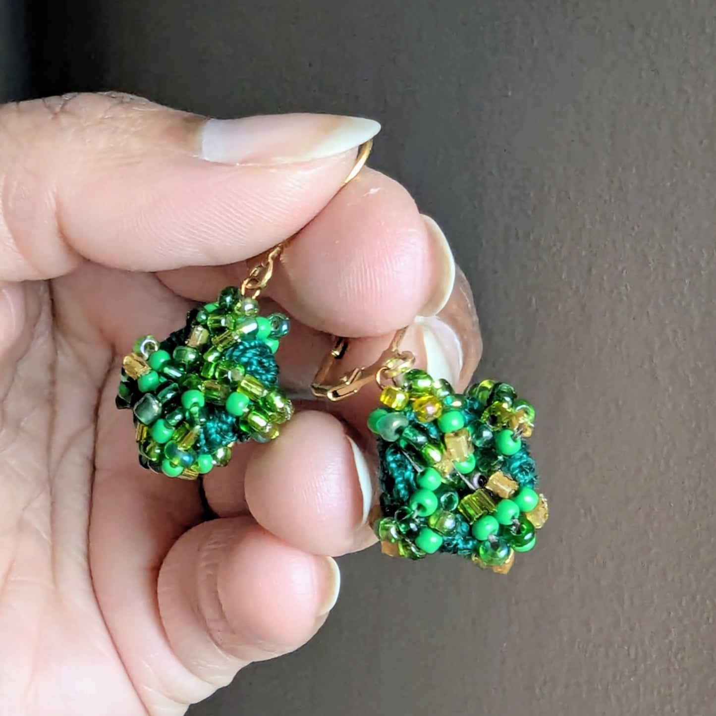 Hand holding a one off everyday pair of handmade bead crochet earrings designed and sustainably handcrafted in the UK.