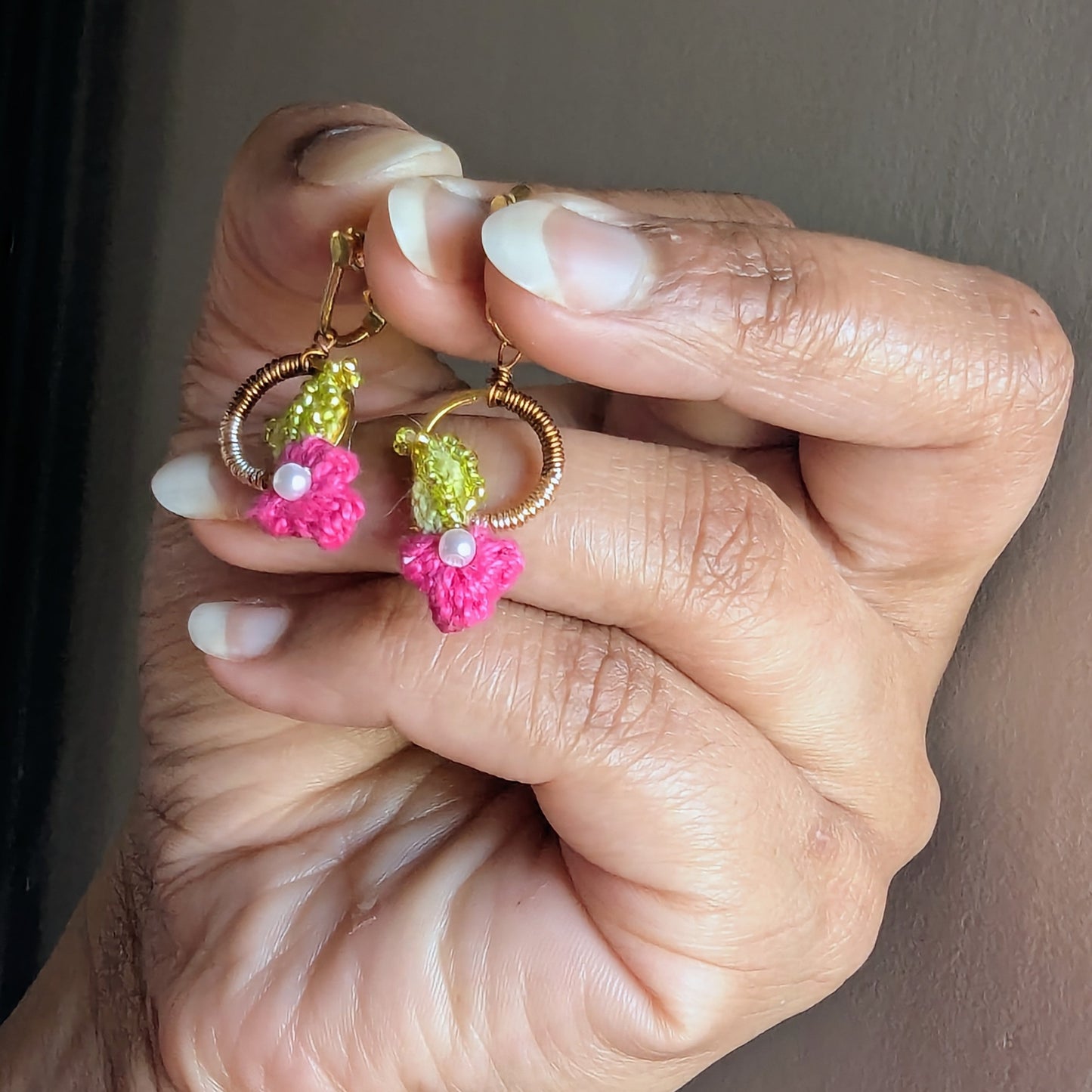Side view of a handmade delicate pair of pink floral clip-on earrings with chartreuse green, gold, bronze and pearl accents featuring a combination of hand crochet, hand bead embroidery and hand wire wrapping artistry unique to Mayaani Jewellery UK and the work of UK designer and artisan Megha.