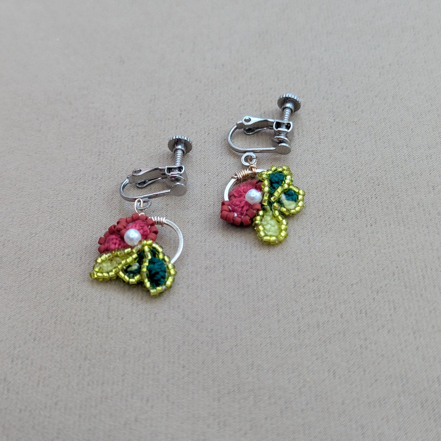Reva handmade clip-on earrings flat lay - rose pink and chartreuse crochet flower pair by Mayaani Jewellery UK.