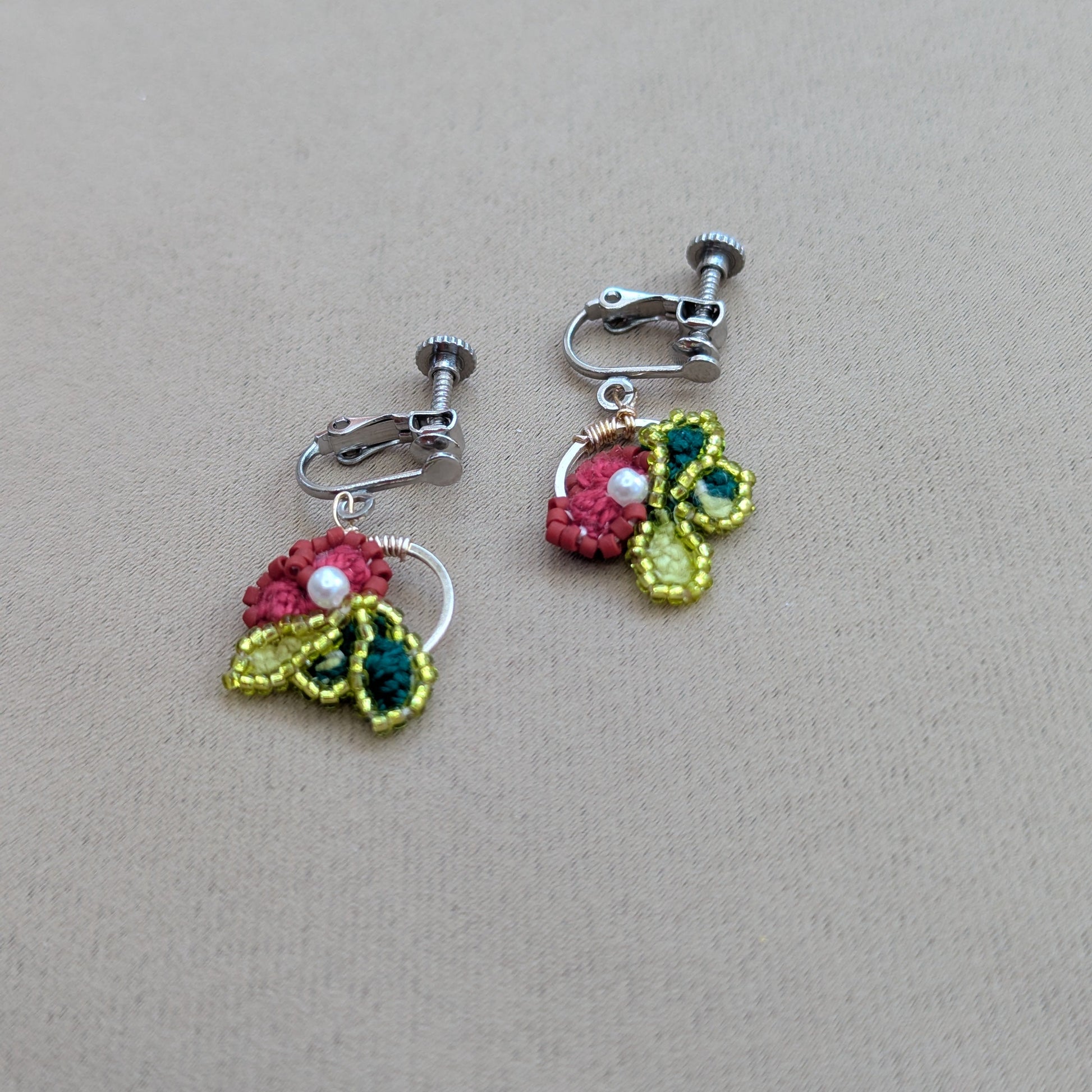 Reva handmade clip-on earrings flat lay - rose pink and chartreuse crochet flower pair by Mayaani Jewellery UK.