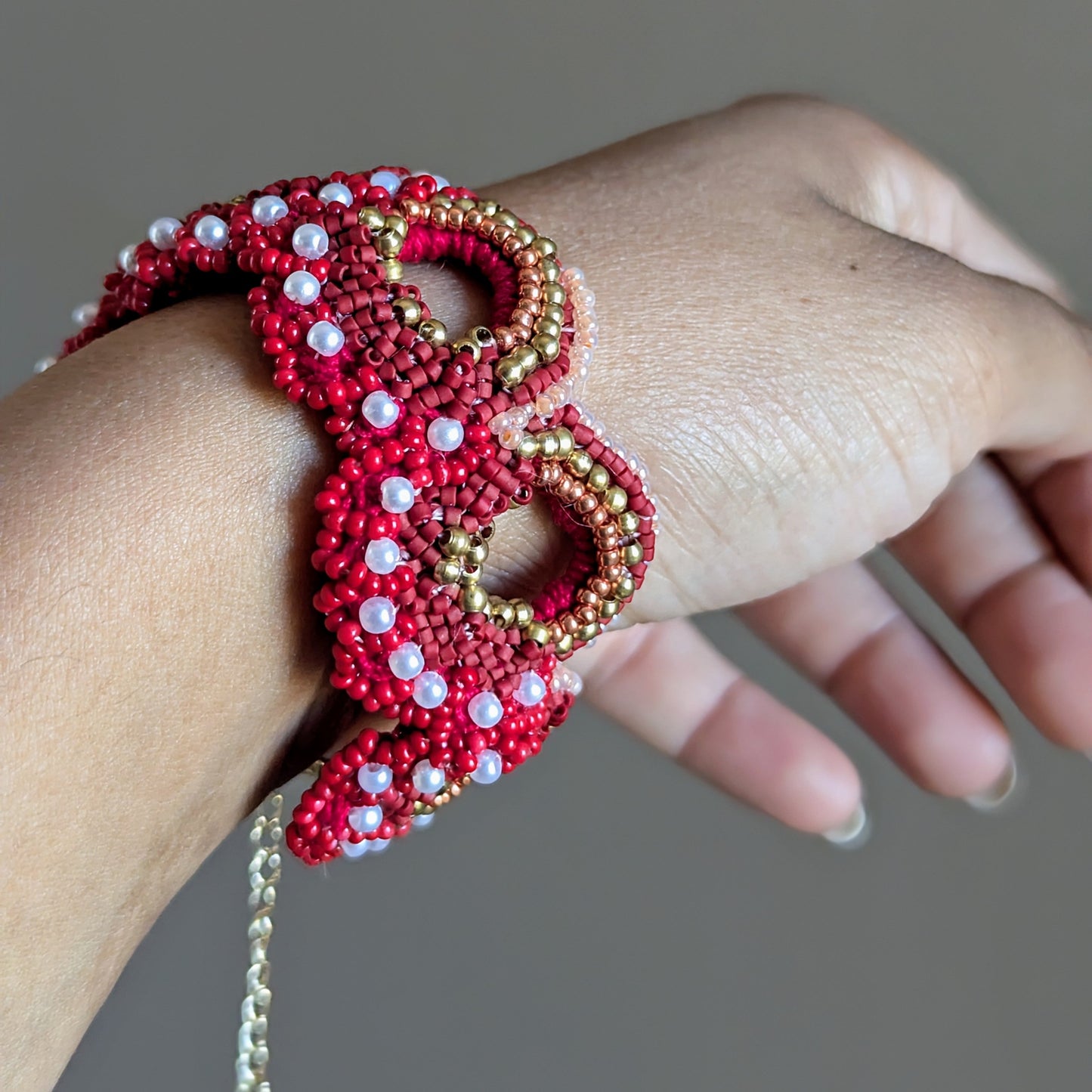 Close up of the Shreya 5-in-1 Western style bracelet worn on a wrist featuring intricate beadwork in red with gold and pearl accents.