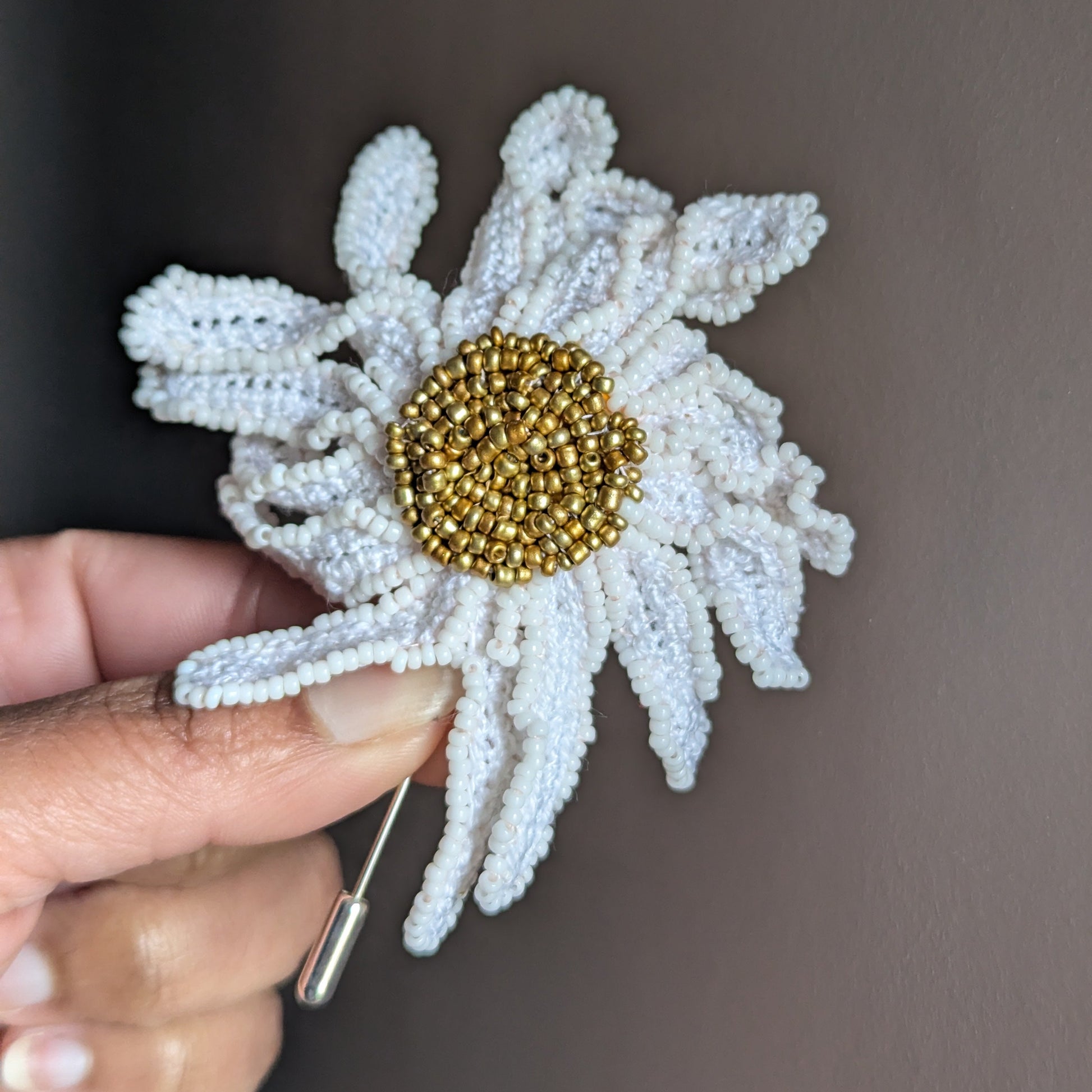 A hand holding a large detailed gold and white daisy flower stick pin brooch/ lapel/ hat accessory intuitively designed and expertly handmade at Mayaani Jewellery UK.