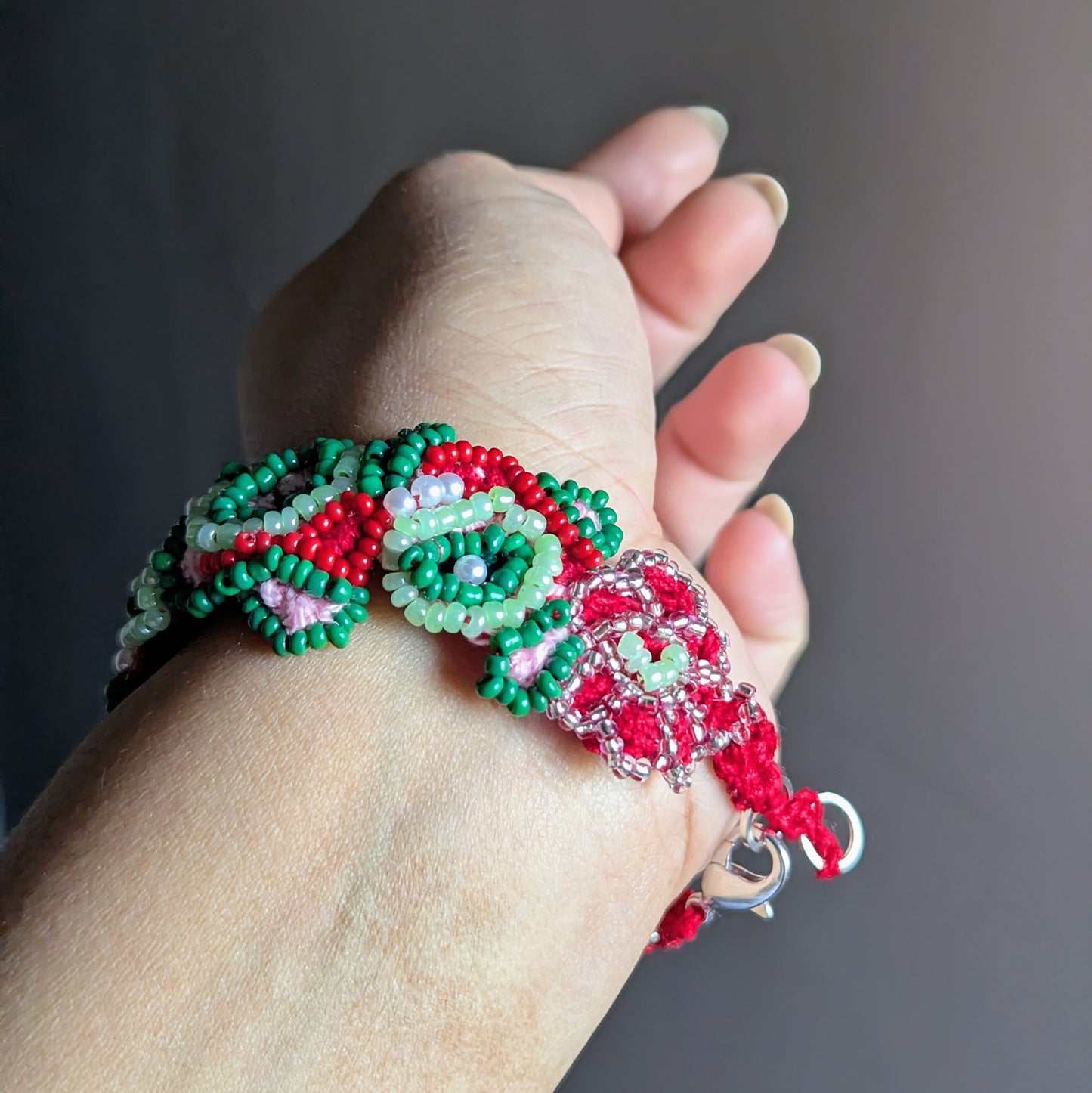 Green, red and pink artisan beaded bracelet held in hand, featuring vintage pearls and Miyuki beads.