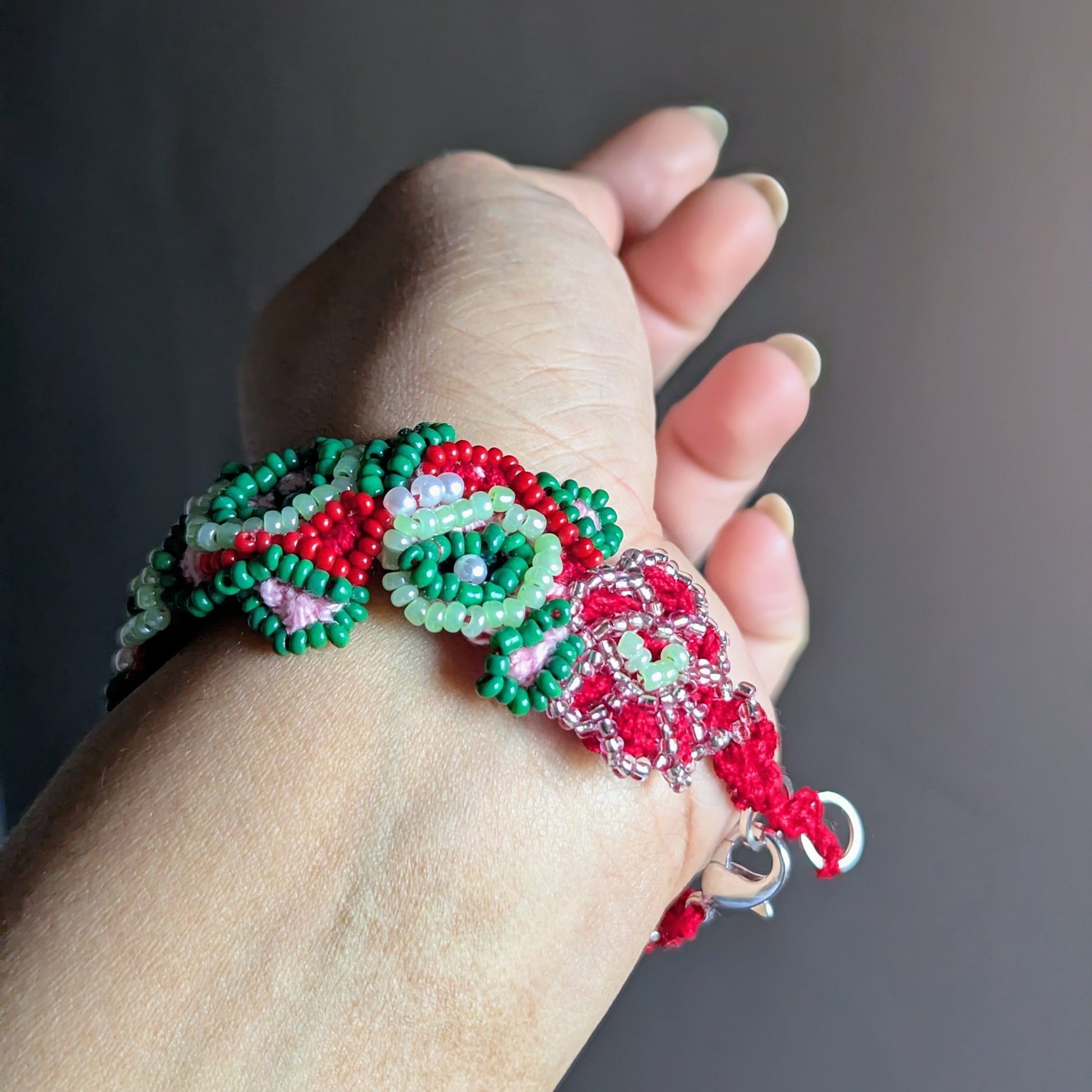Green, red and pink artisan beaded bracelet held in hand, featuring vintage pearls and Miyuki beads.