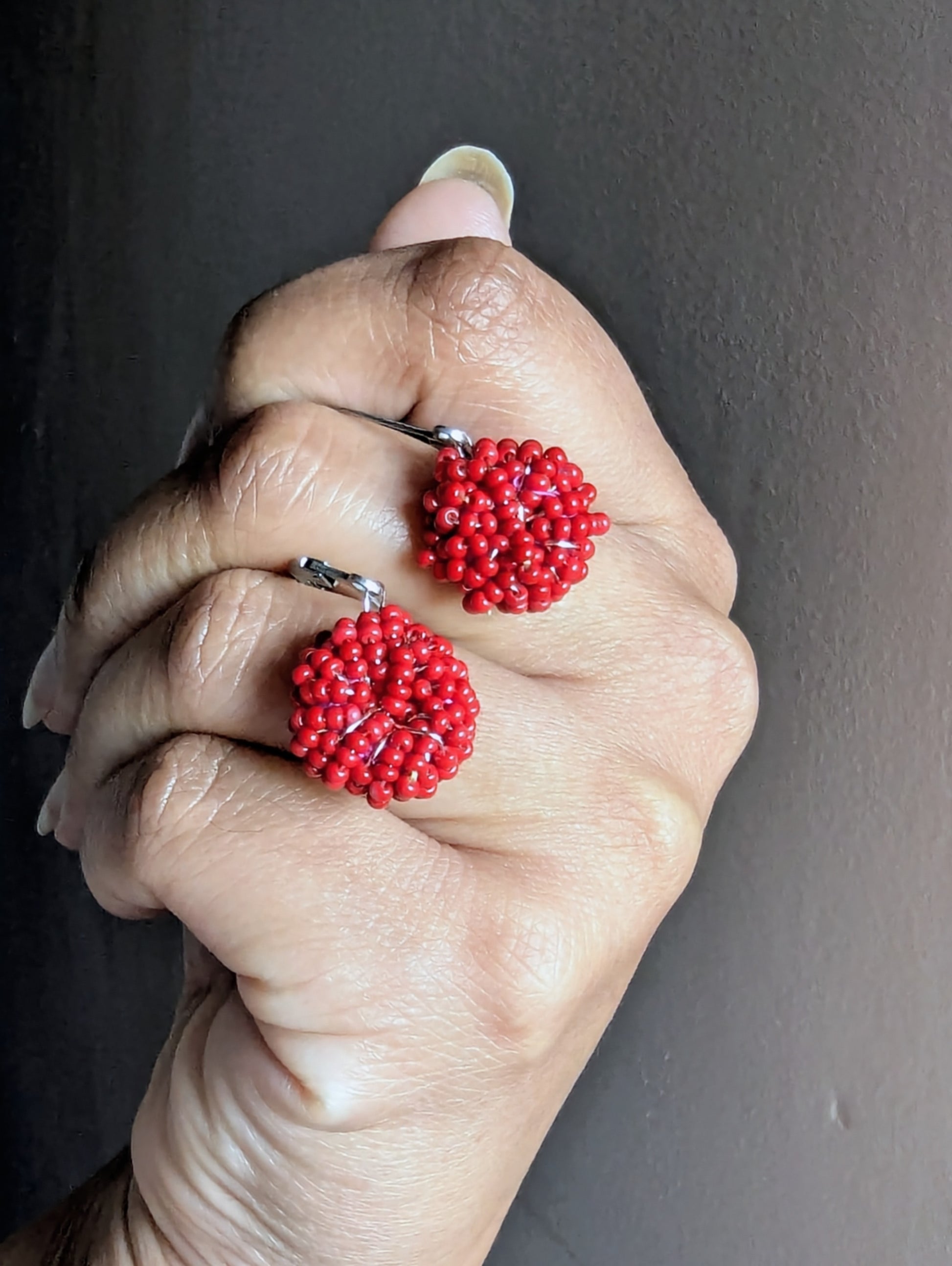 Close-up of Malika Masi red beaded earrings showing intricate beadwork and stainless-steel clasps.