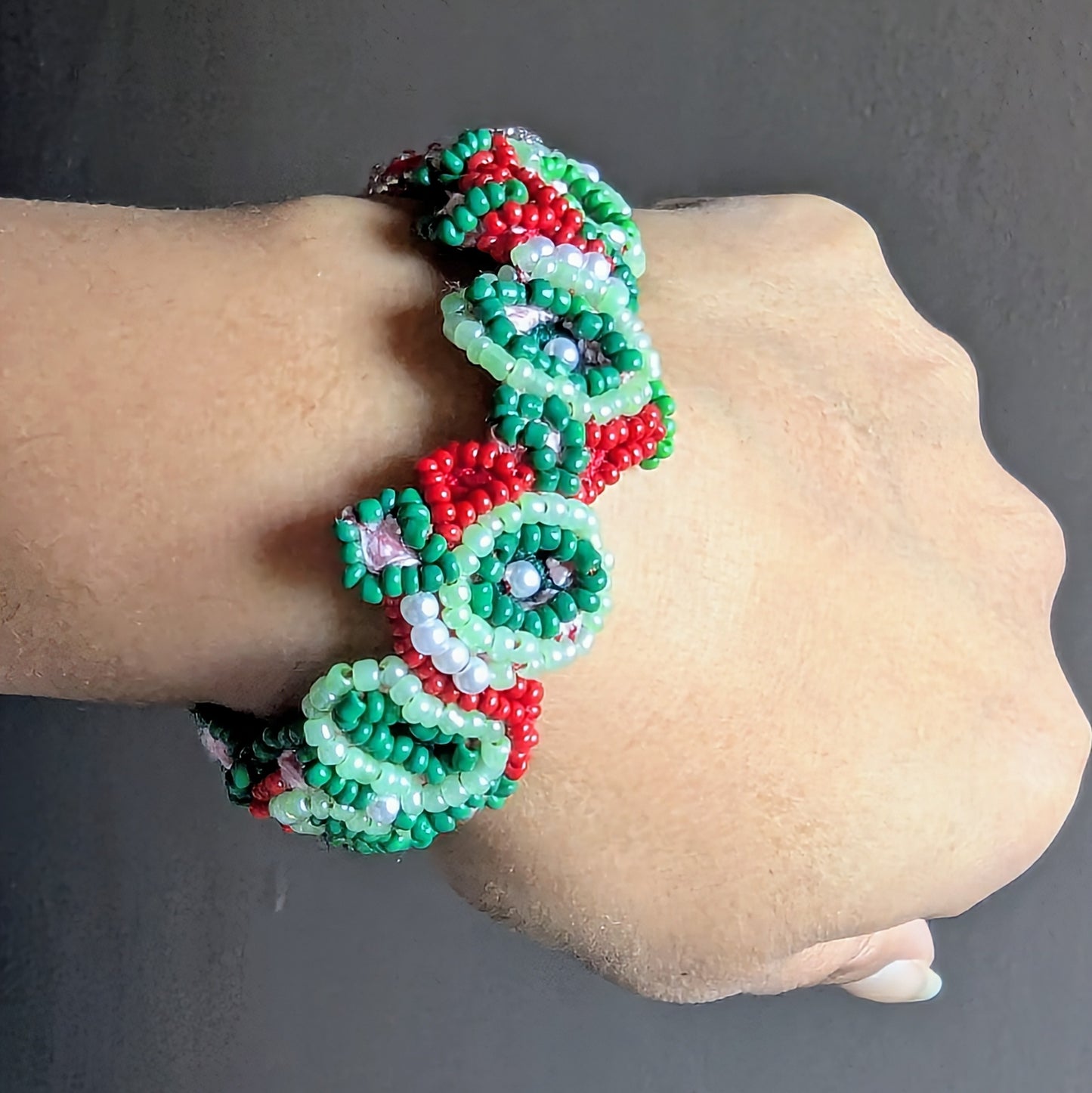 Beaded bracelet with green and red pattern on a wrist against a grey background