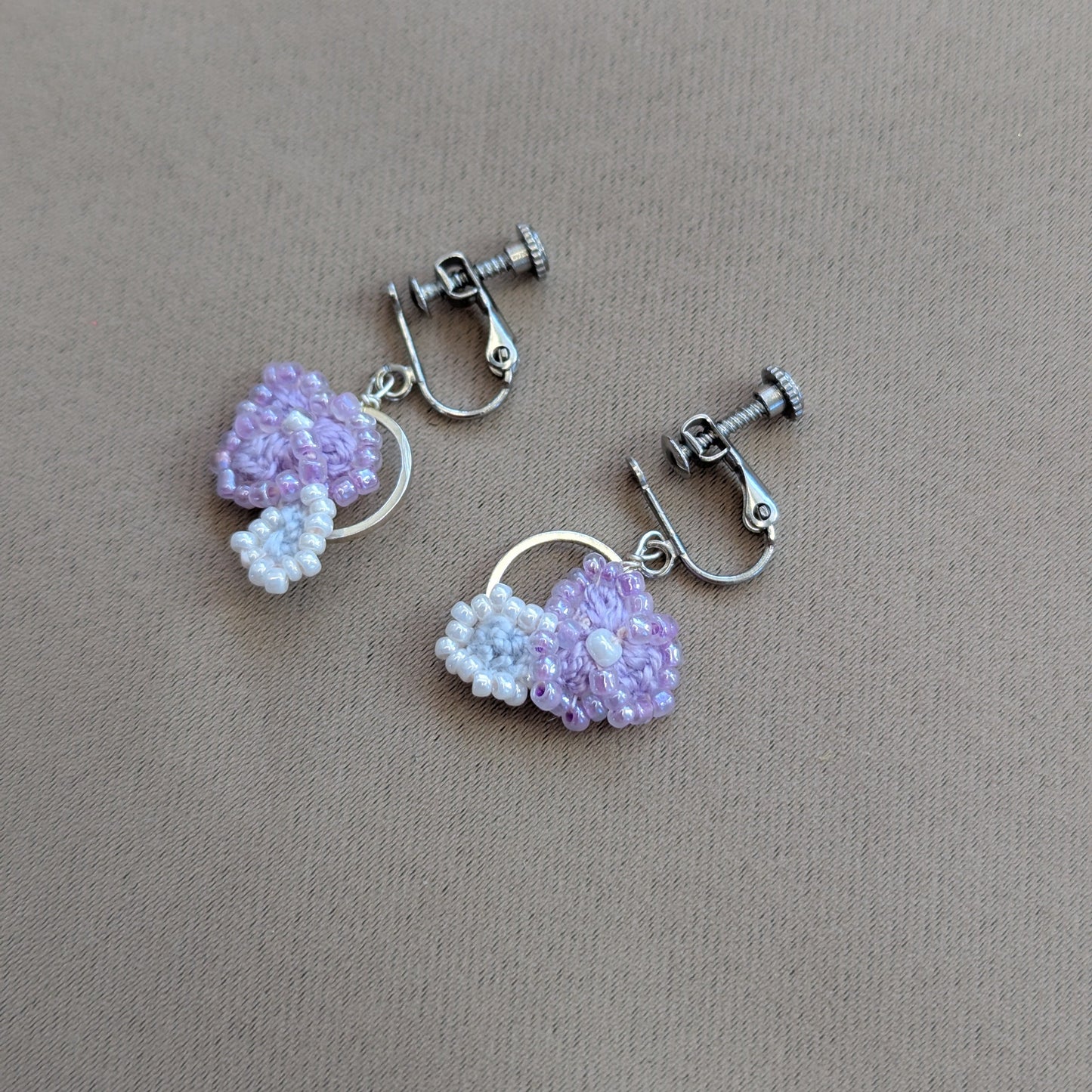 One-of-a-kind djustable clip-on Malti lilac and silver earrings exclusive to Mayaani lying on a neutral grey backdrop.