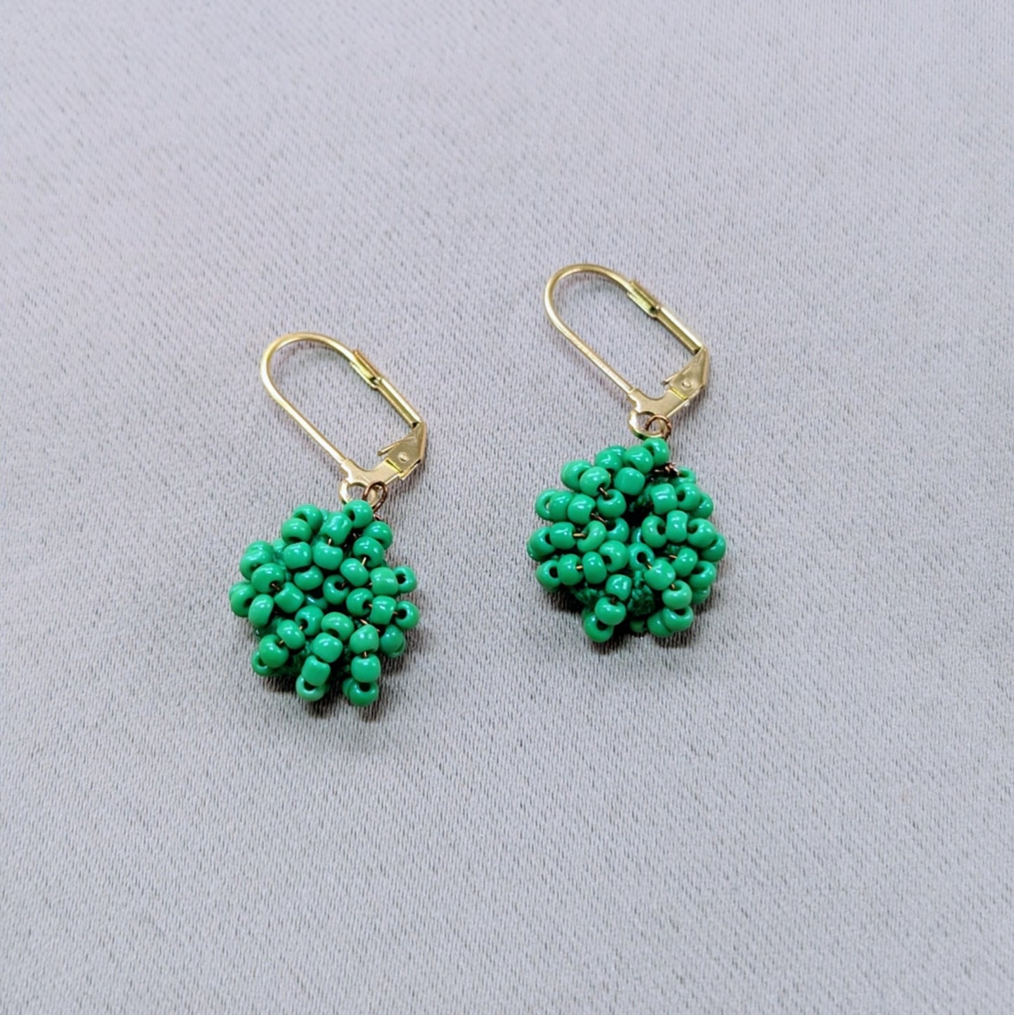 Pair of bright green seed bead earrings held in hand, handcrafted by Indian artisan Megha.