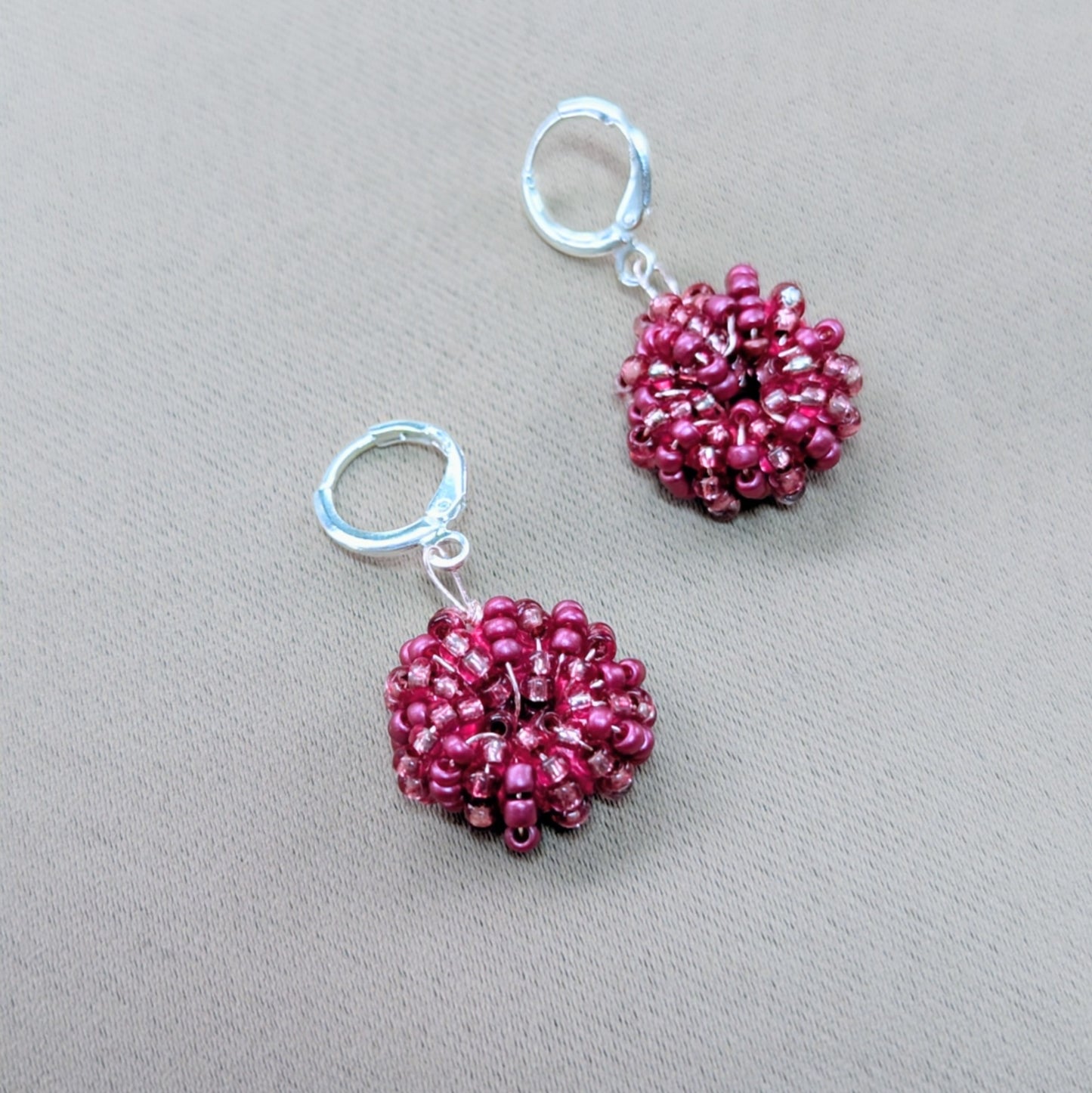 Small round pink handmade earrings held between fingers, glowing softly in natural light.